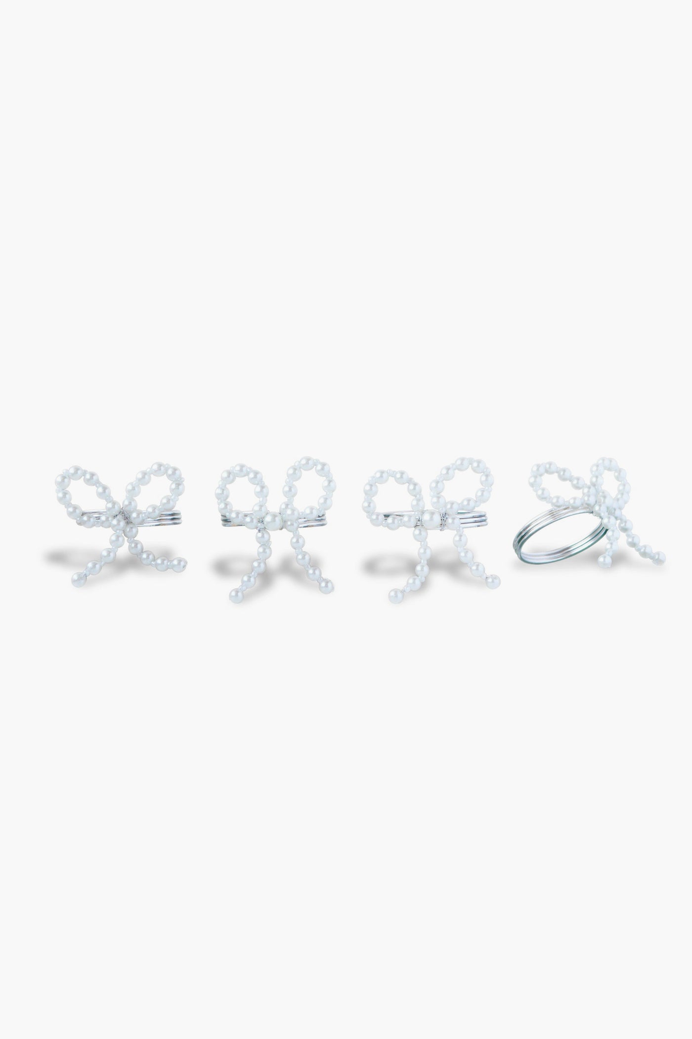 The Chefanie Pearl Bow Napkin Rings set features four white beaded rings shaped like bows, arranged in a row, perfect for adding elegant charm to your table decor.