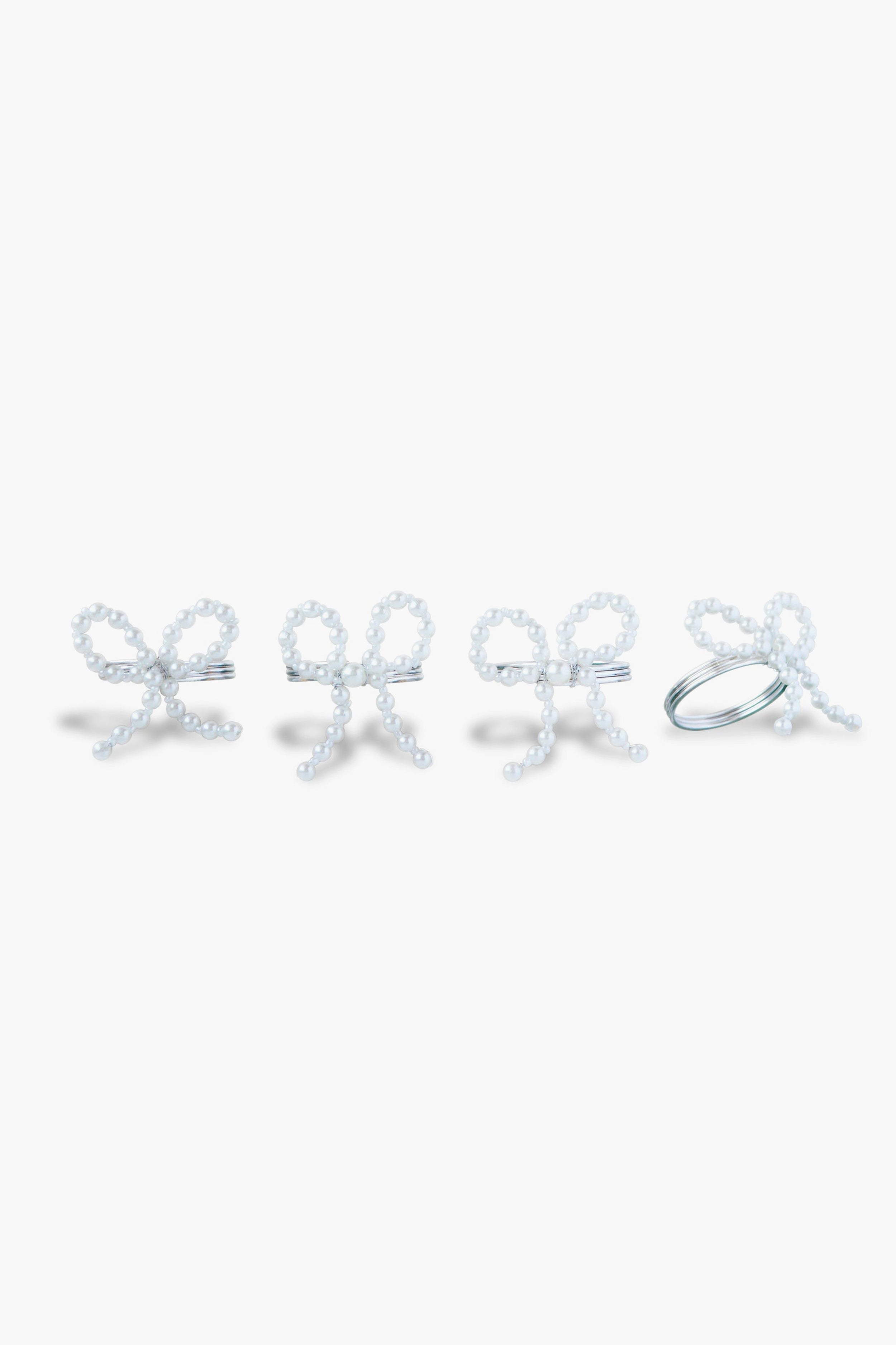 The Chefanie Pearl Bow Napkin Rings set features four white beaded rings shaped like bows, arranged in a row, perfect for adding elegant charm to your table decor.