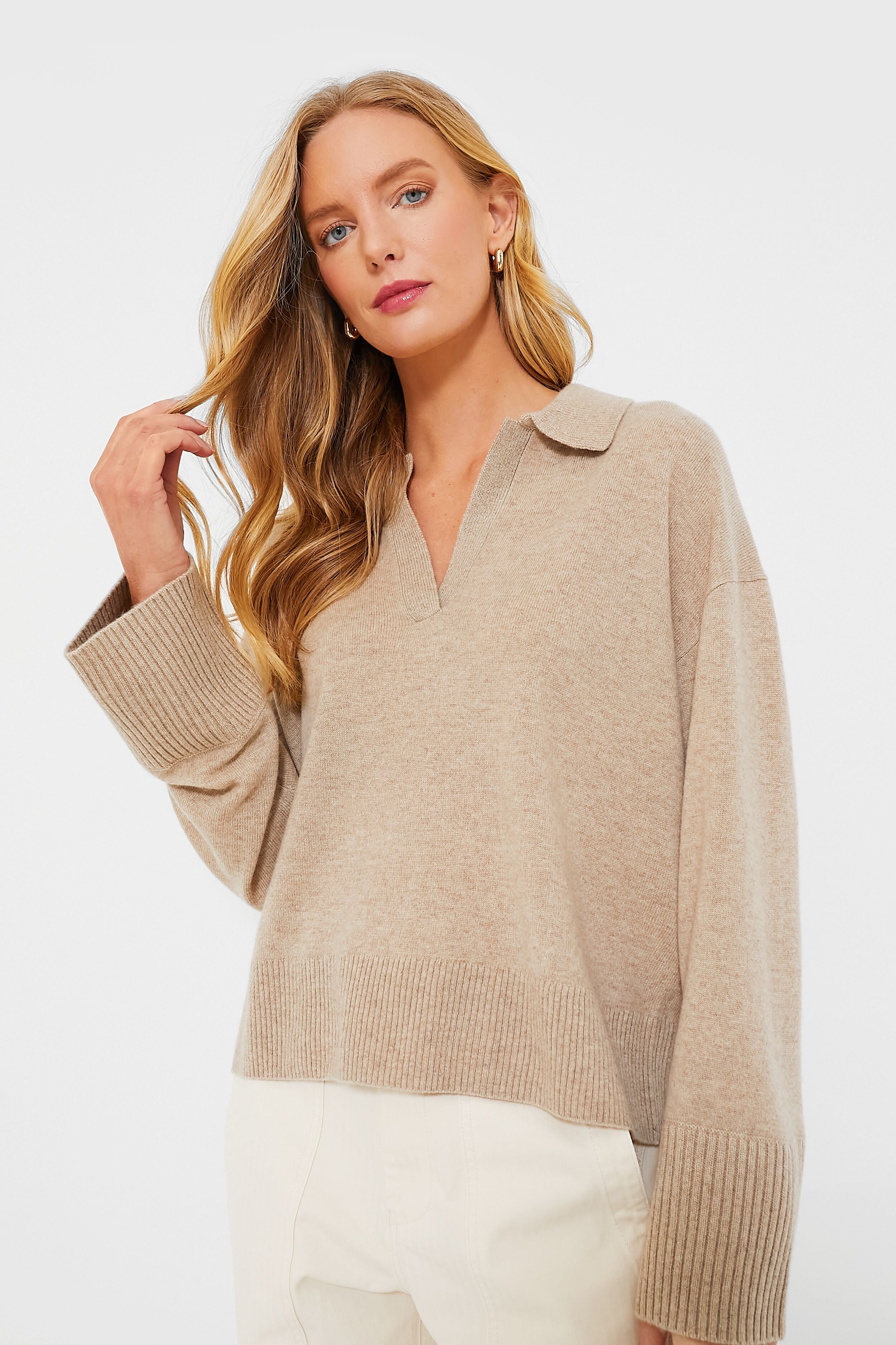 A woman with long blonde hair wears a beige Alex Mill women's cashmere sweater and white pants, highlighting a classic essential sweater style.