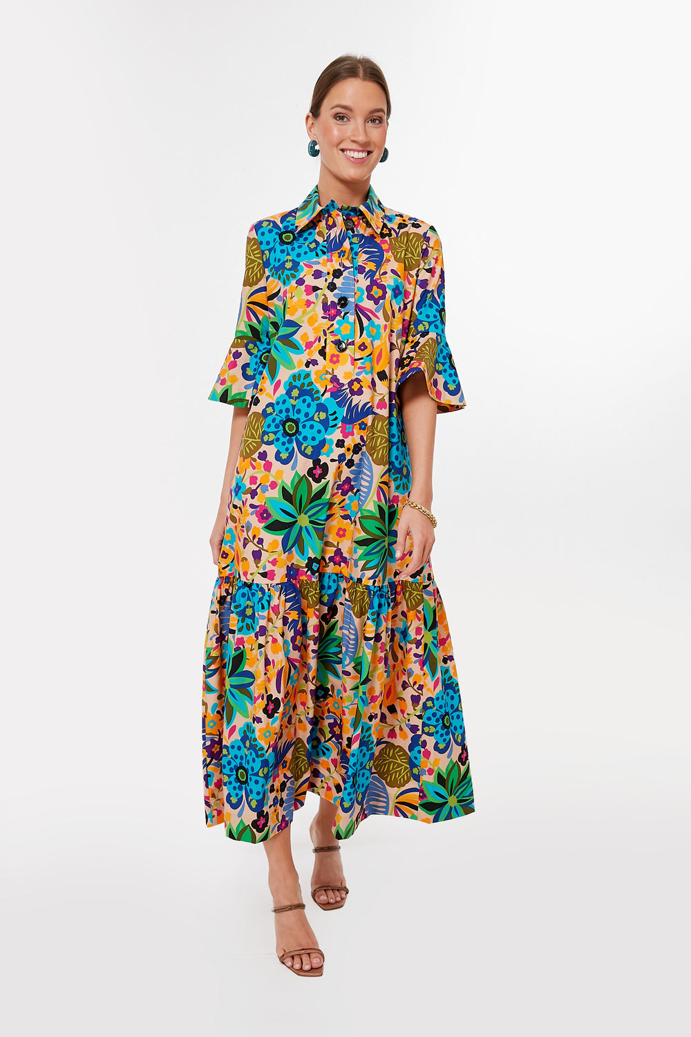 A woman smiles brightly wearing the La DoubleJ Maui Artemis Dress, a colorful floral-print collared maxi with short sleeves. Made in Italy.