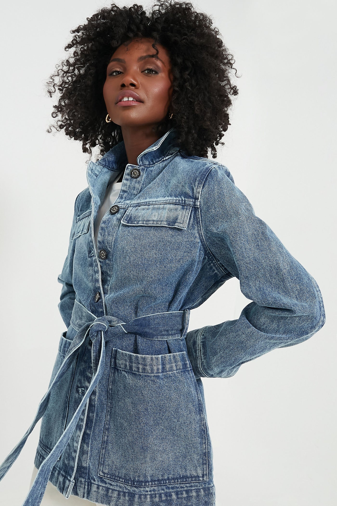 A woman in a Barbour belted denim jacket with chest pockets and button closures, styled like an Indigo Chambray Barbour overshirt—an iconic women’s outerwear piece.
