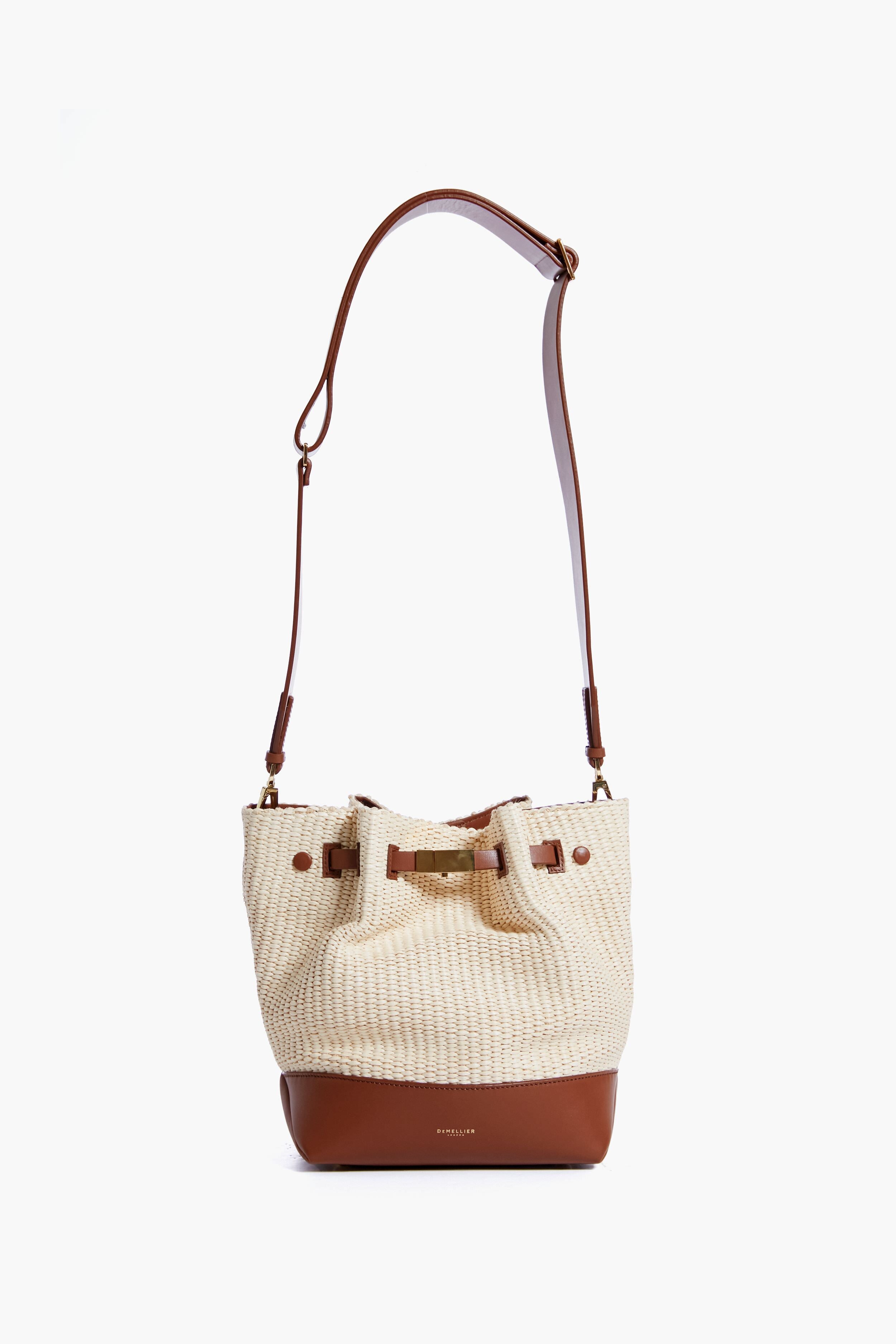 The Demellier straw and brown leather bucket bag features an adjustable shoulder strap and drawstring closure, showcasing the brand's expert craftsmanship.