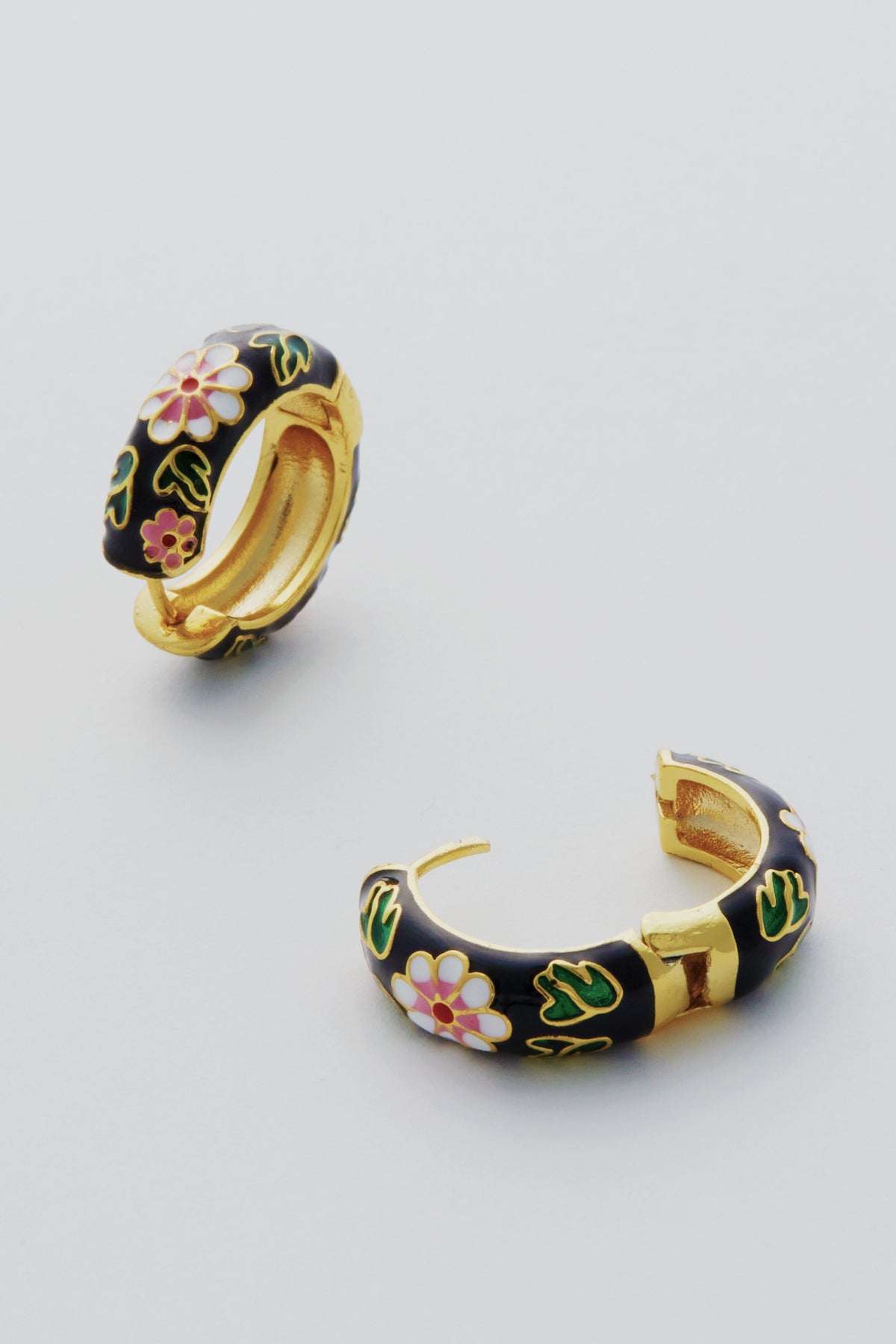 Petit Moments’ Black Deco Hoops are gold-plated with black enamel, adorned with pink and white flowers and green leaves, adding a touch of floral elegance to any look.