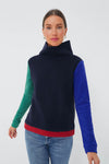 Woman wears a Dudley Stephens colorblock pullover sweater with a high collar, green and blue sleeves, red hem, and blue jeans. Made from sustainable recycled yarn inspired by the brand’s signature fleece.