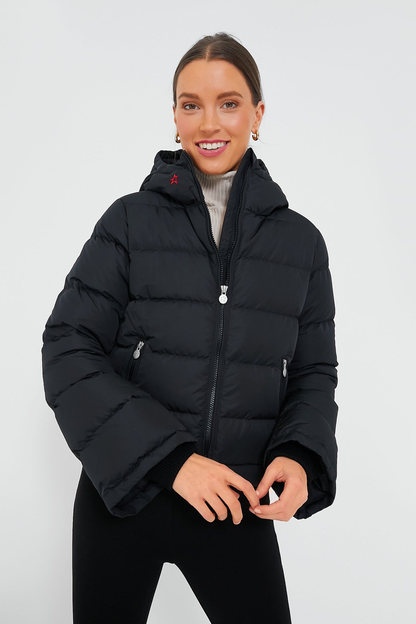 A woman smiles confidently in a Perfect Moment black down-insulated puffer jacket over a light turtleneck.