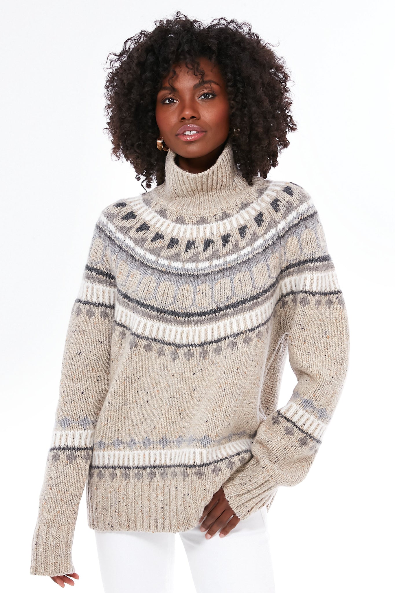 A person in an oatmeal combo apres ski turtleneck and white pants confidently showcases the Alex Mill beige and gray Donegal knit sweater featuring a cozy Fair Isle design.