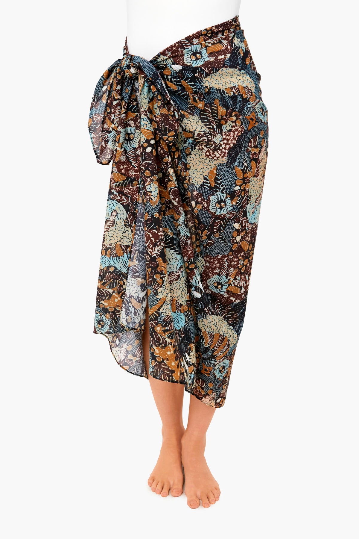 Wearing a knee-length Ulla Johnson batik sarong with a large side bow and brown, blue, and beige floral print—a stylish cotton coverup or lightweight swimwear for chic days by the water.