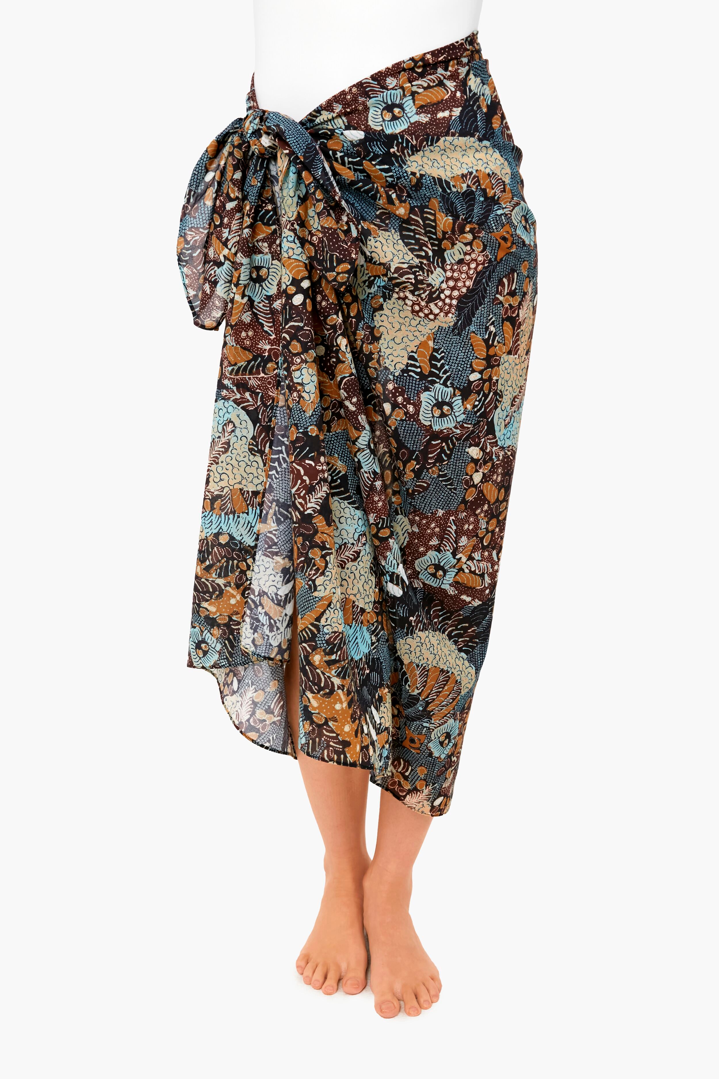 Wearing a knee-length Ulla Johnson batik sarong with a large side bow and brown, blue, and beige floral print—a stylish cotton coverup or lightweight swimwear for chic days by the water.