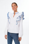A woman wears a Hyacinth House white ruffle blouse with blue-trimmed shoulder ruffles and long sleeves, paired with blue jeans.