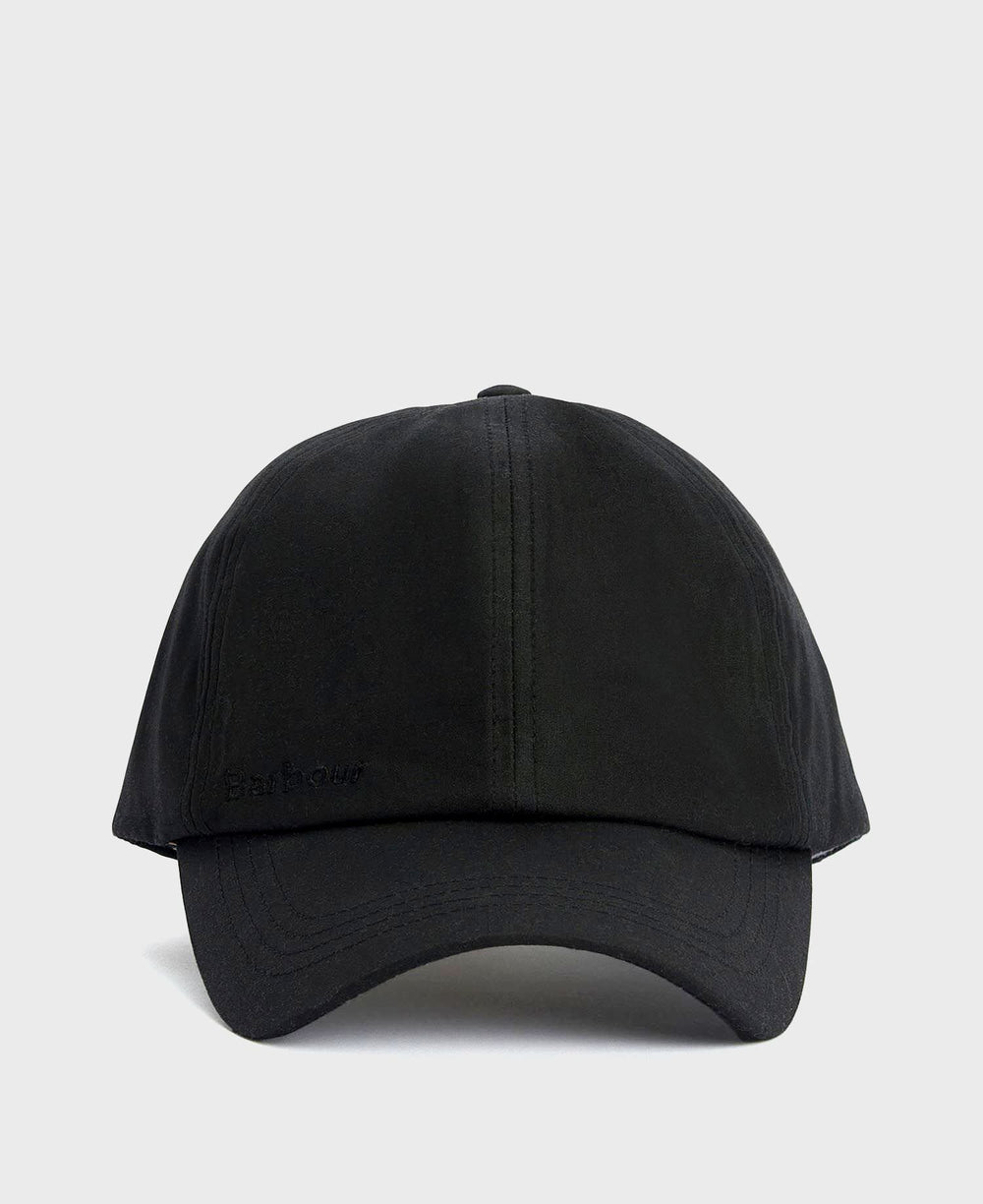 A Barbour black waxed cotton cap with a timeless look and water-resistant finish is displayed in a neutral, minimal setting.