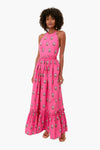A woman stands wearing the RHODE hot pink floral maxi dress with a halter neckline, ruffled hem, and paired with sandals.