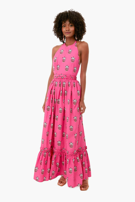 A woman stands wearing the RHODE hot pink floral maxi dress with a halter neckline, ruffled hem, and paired with sandals.