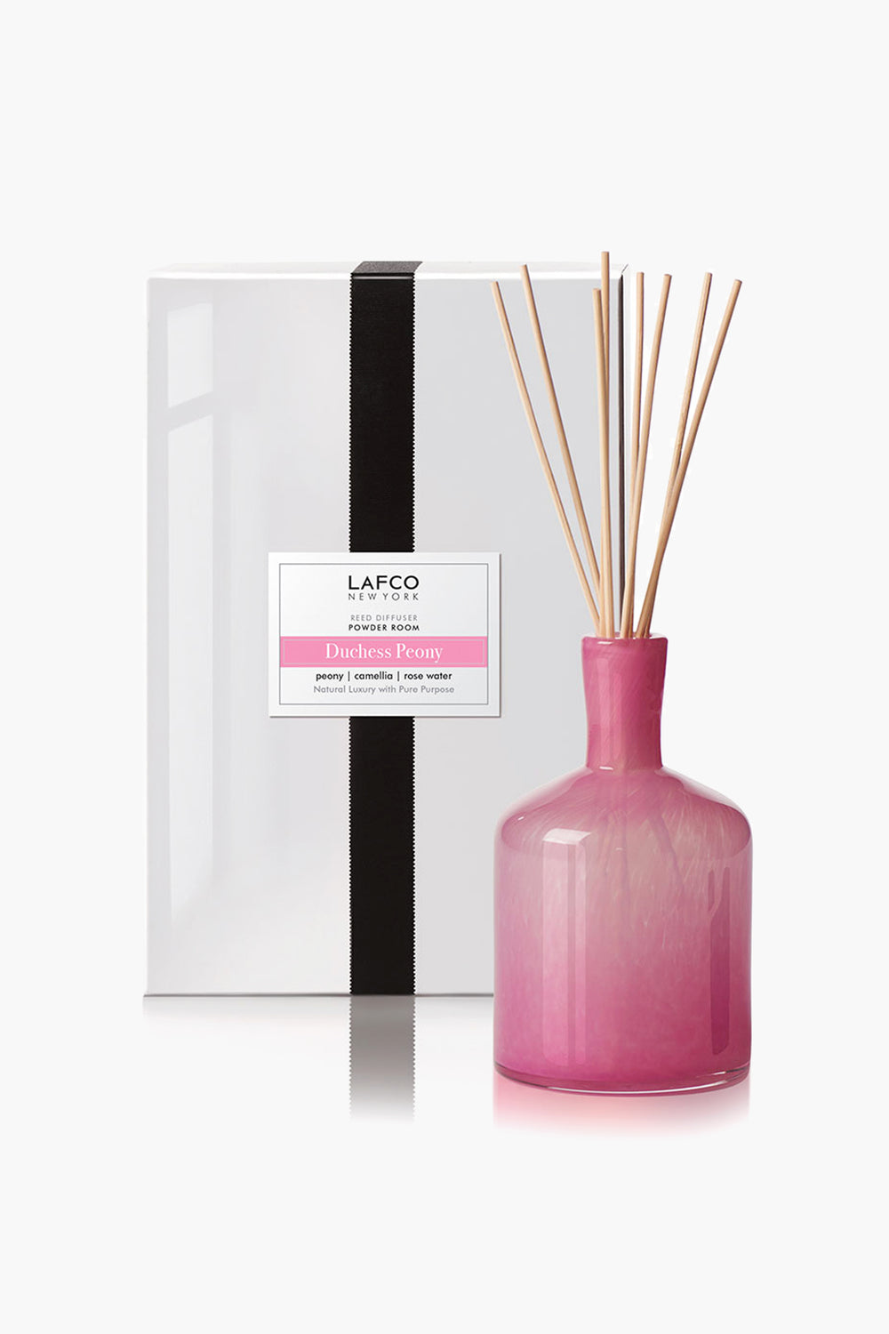 A pink glass reed diffuser with wooden reeds by LAFCO New York stands beside a white Duchess Peony gift box, ideal for lovers of luxury candles.