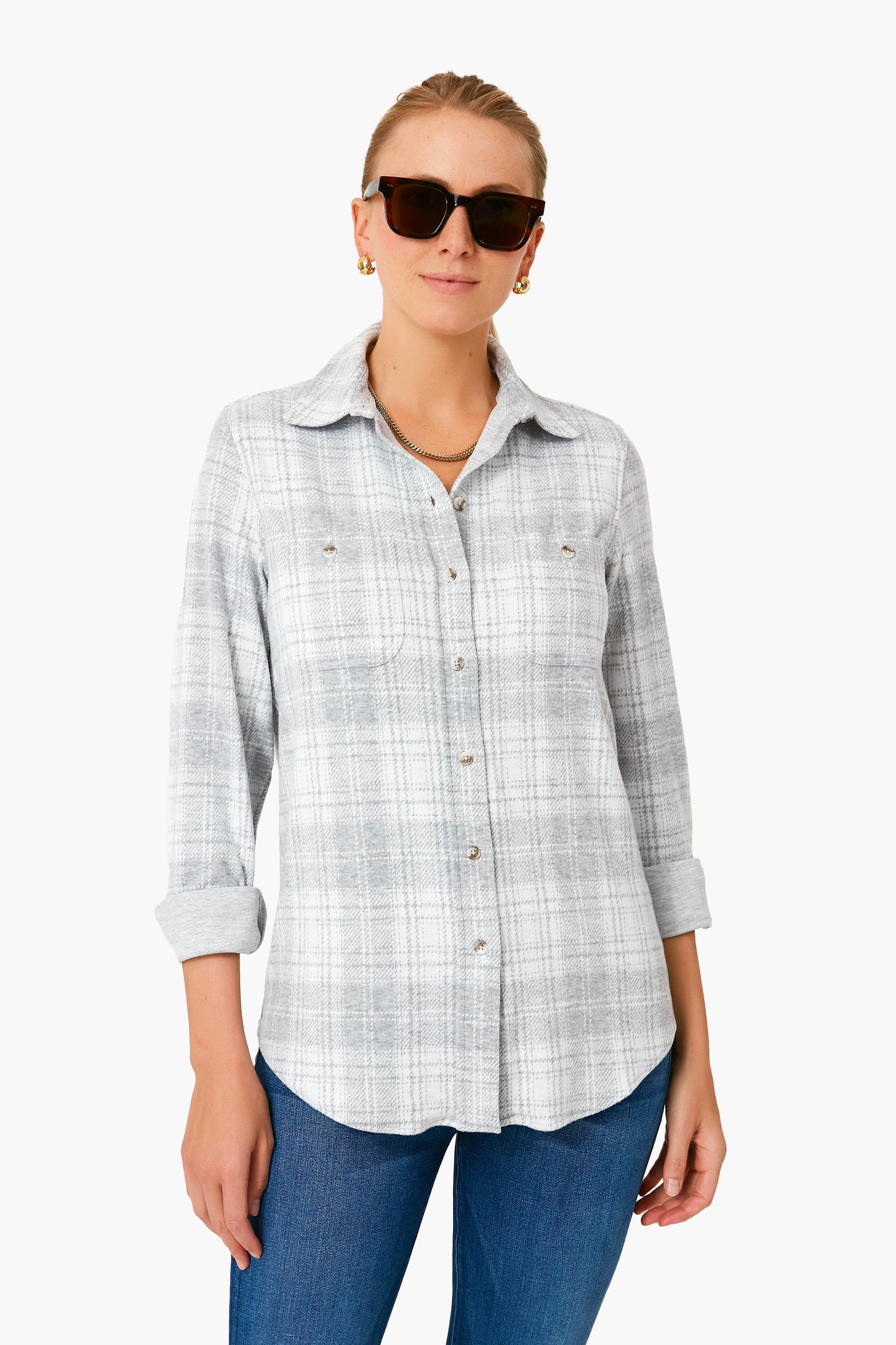 Woman wearing dark sunglasses, gold jewelry, blue jeans, and a Faherty light grey plaid sweater shirt with rolled sleeves—an effortless take on sustainable apparel.
