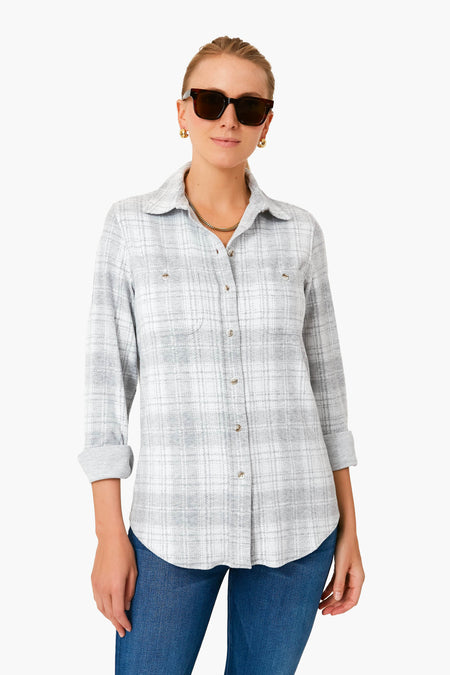 Woman wearing dark sunglasses, gold jewelry, blue jeans, and a Faherty light grey plaid sweater shirt with rolled sleeves—an effortless take on sustainable apparel.