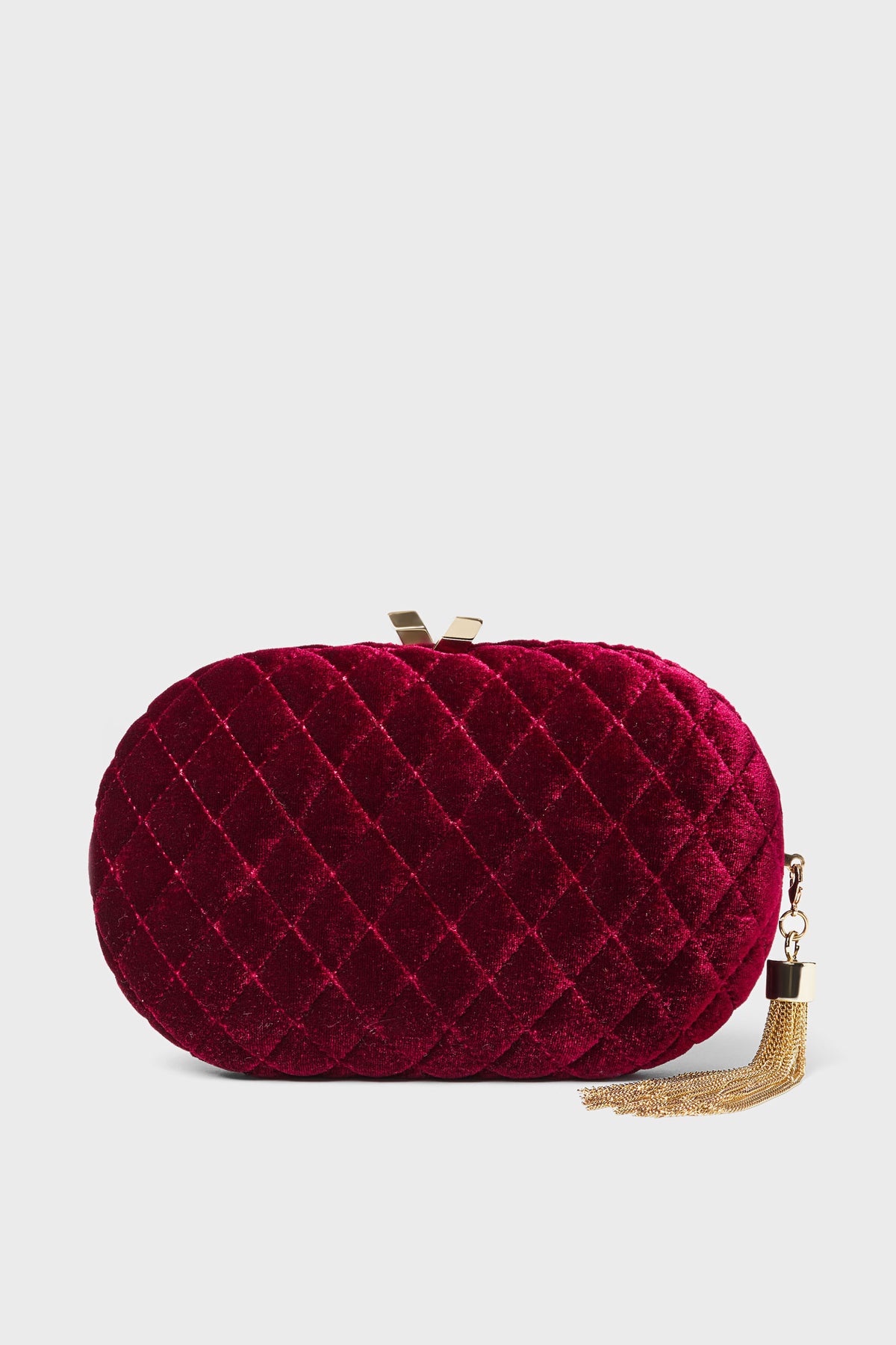 Oval-shaped quilted red velvet clutch evening bag by Olga Berg, accented with a gold clasp and a gold chain tassel on the side.