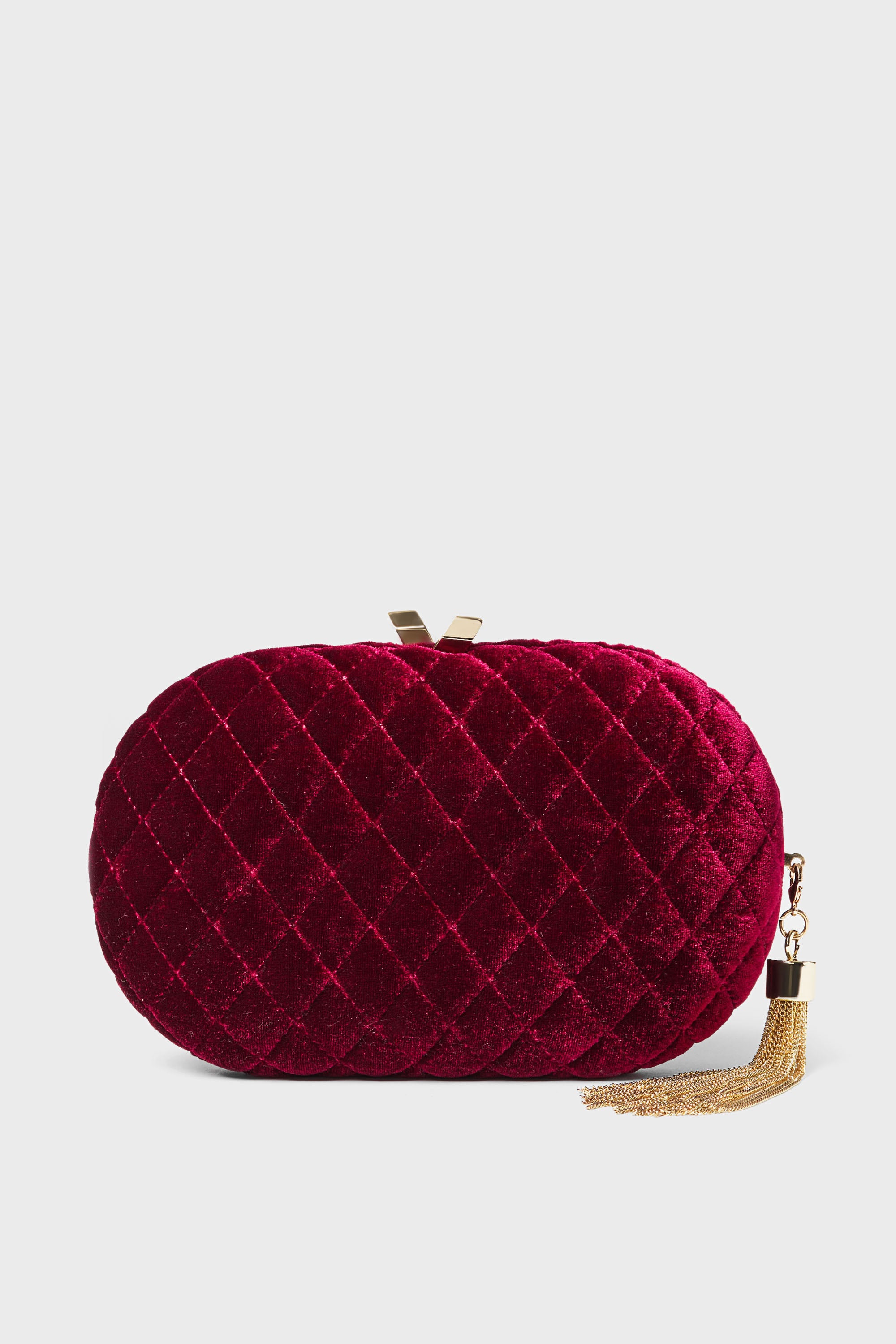 Oval-shaped quilted red velvet clutch evening bag by Olga Berg, accented with a gold clasp and a gold chain tassel on the side.
