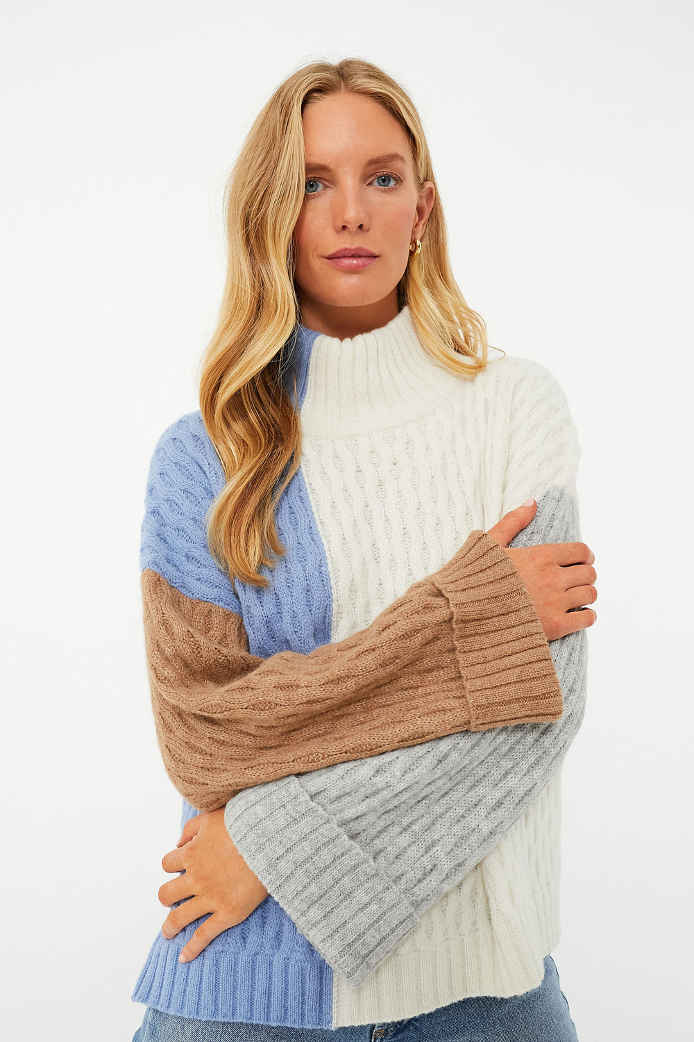 A woman with long blonde hair wears the ELEVEN SIX Celia Sweater, a color-blocked knit in cream, light blue, tan, and gray, crafted with Andean knitting techniques.