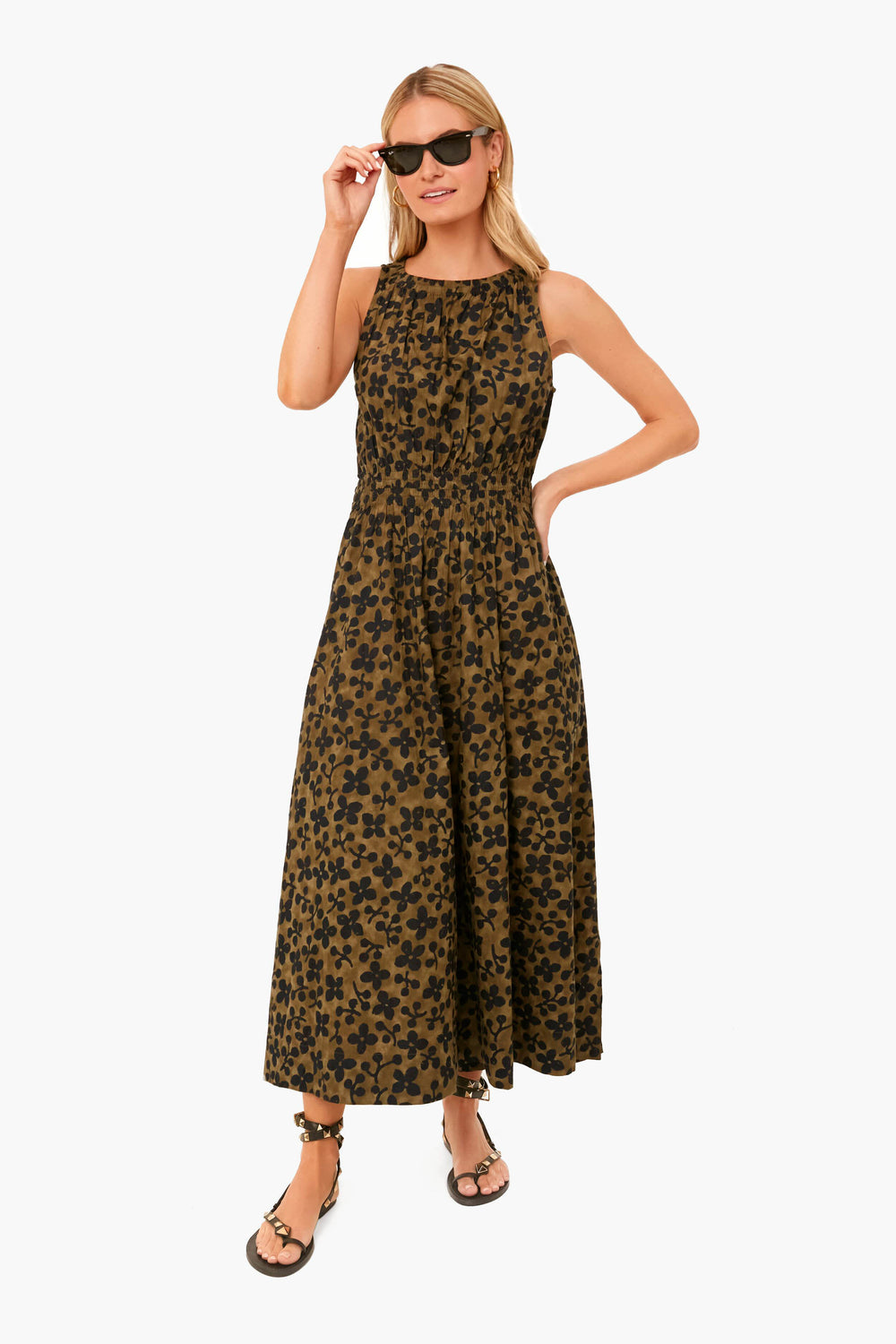 A woman in an Apiece Apart sleeveless, ankle-length floral olive dress pairs it with black sunglasses and sandals for a chic, effortless look.