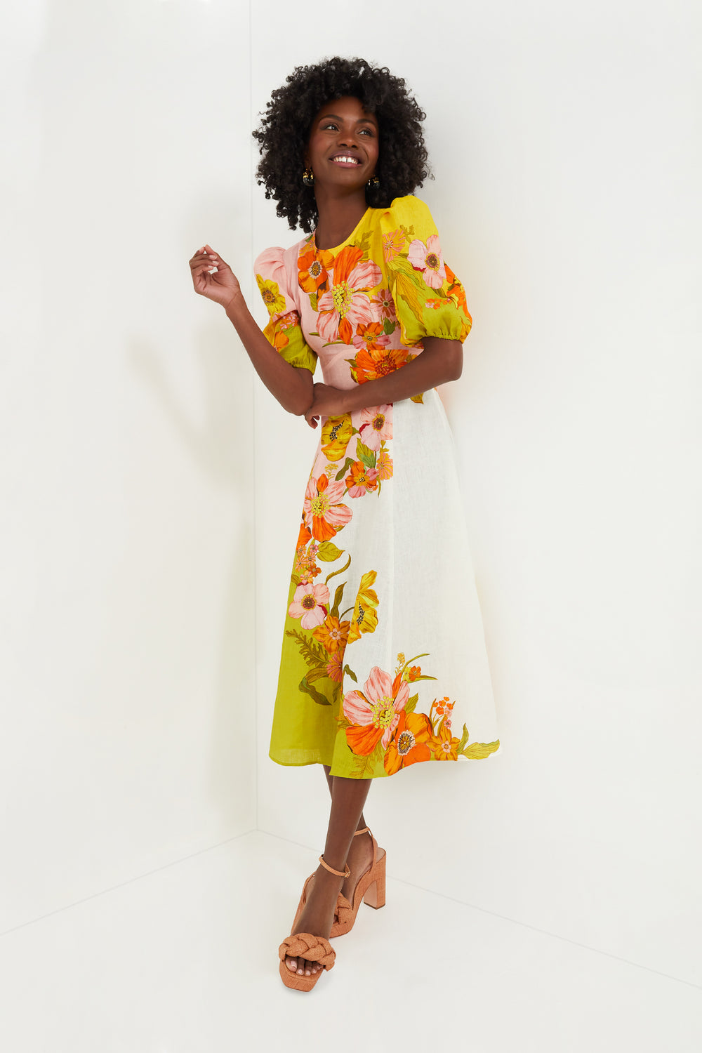 A woman in an Alemais floral midi dress with puff sleeves and tan platform heels smiles brightly, radiating effortless charm.