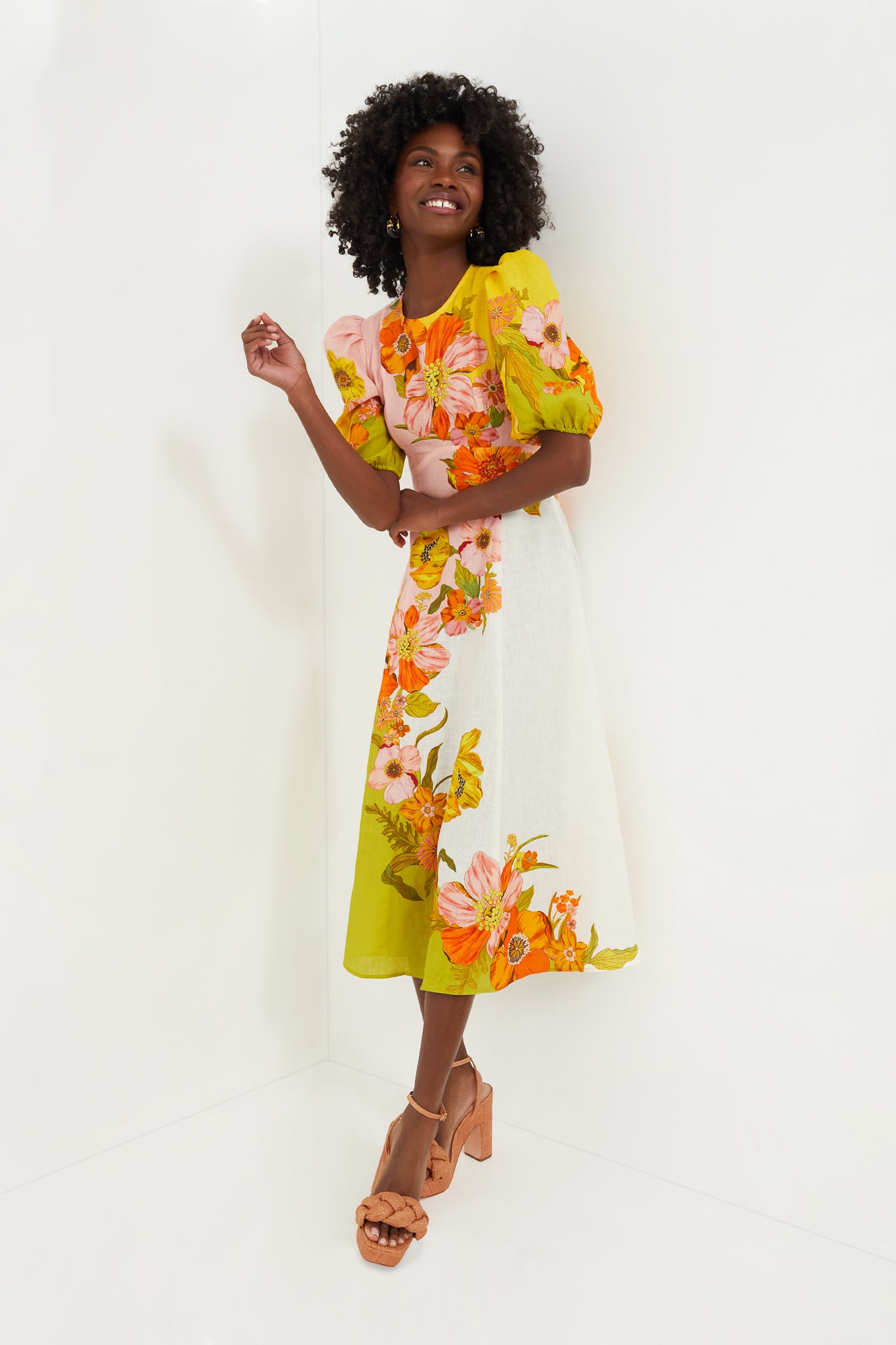 A woman in an Alemais floral midi dress with puff sleeves and tan platform heels smiles brightly, radiating effortless charm.