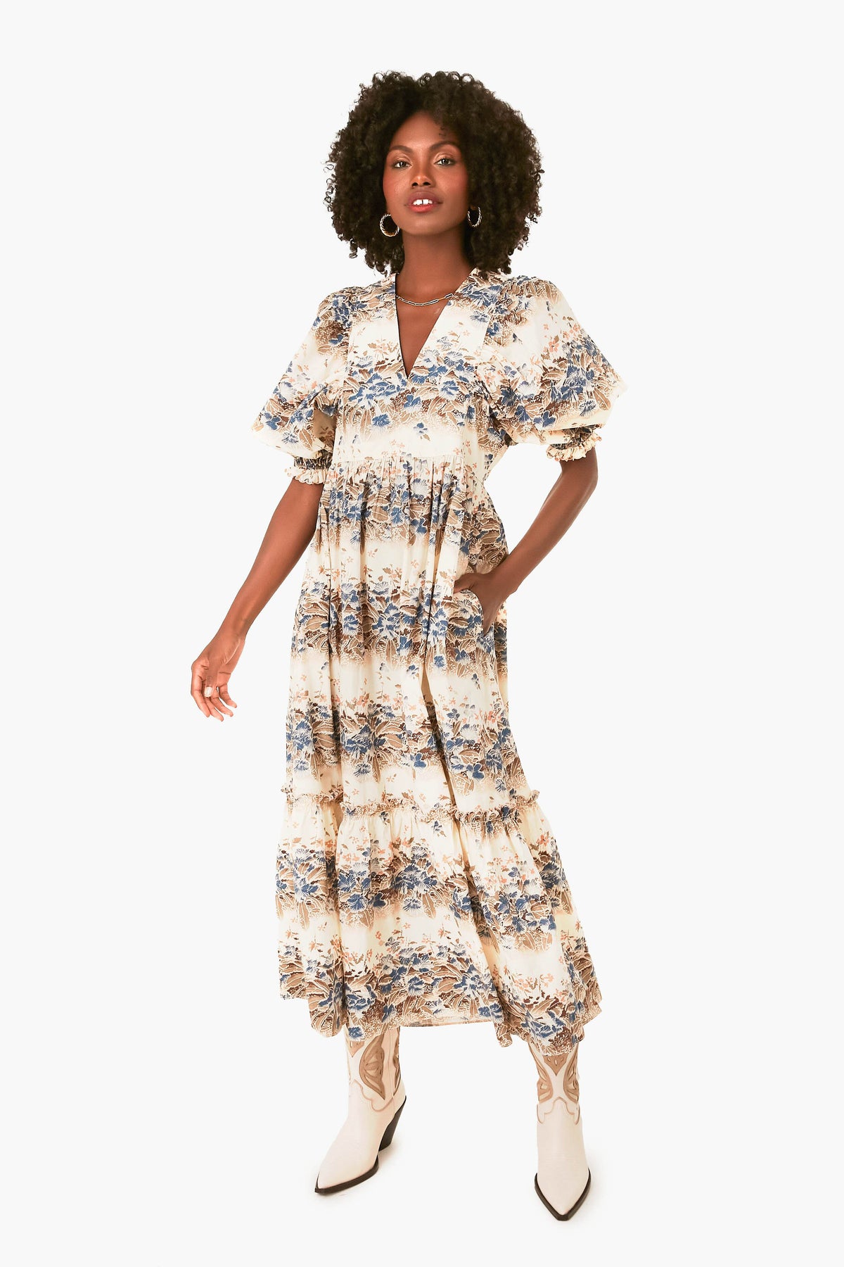 A woman wears a Hunter Bell ankle-length cotton poplin dress featuring short ruffled sleeves and tiered ruffles, paired with white cowboy boots for a stylish look.