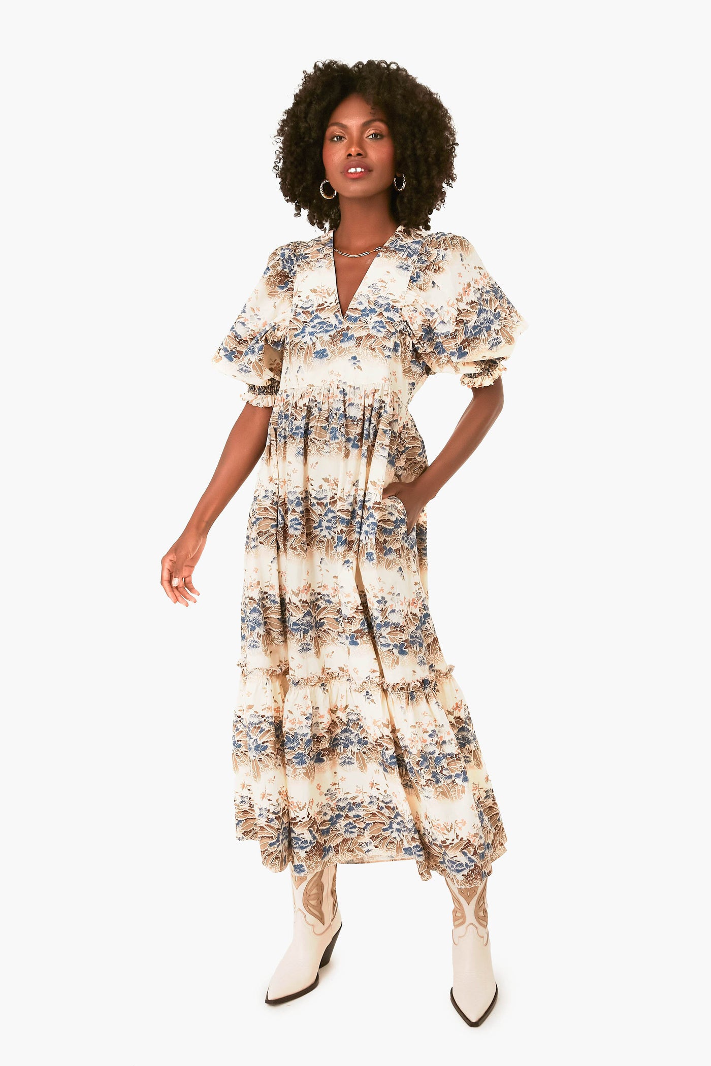 A woman wears a Hunter Bell ankle-length cotton poplin dress featuring short ruffled sleeves and tiered ruffles, paired with white cowboy boots for a stylish look.