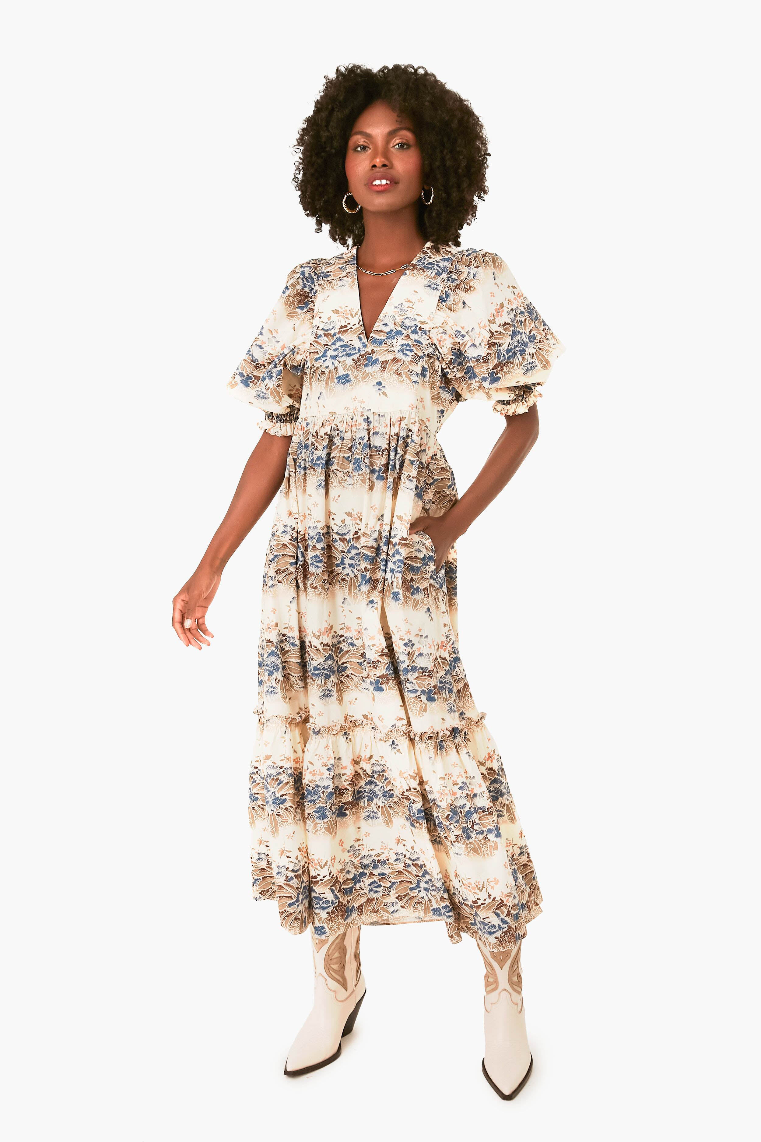 A woman wears a Hunter Bell ankle-length cotton poplin dress featuring short ruffled sleeves and tiered ruffles, paired with white cowboy boots for a stylish look.