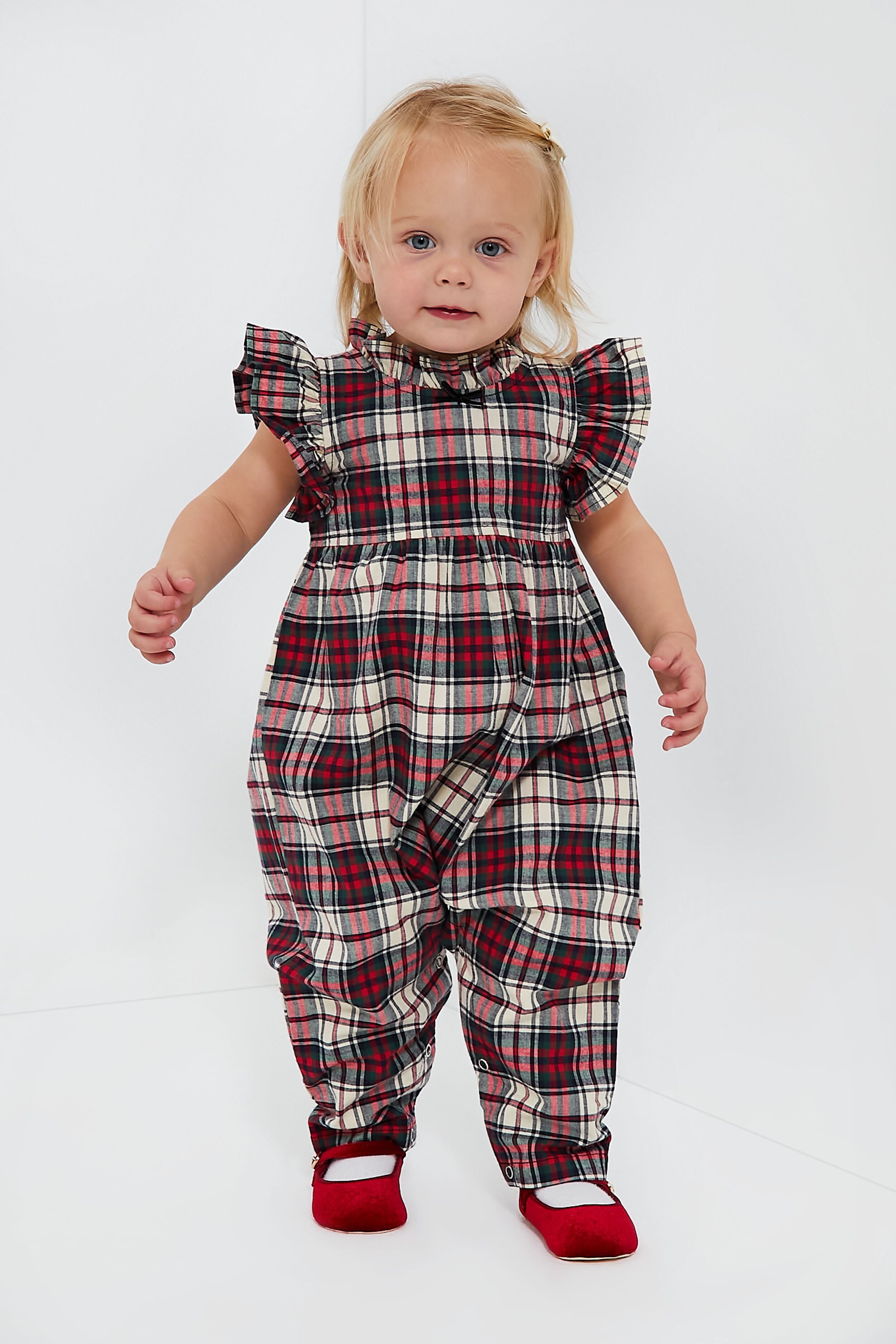 A toddler wears a Pink Chicken Jennifer Jumper made of brushed cotton with red, white, and black plaid, ruffled sleeves and neckline, paired with red shoes.