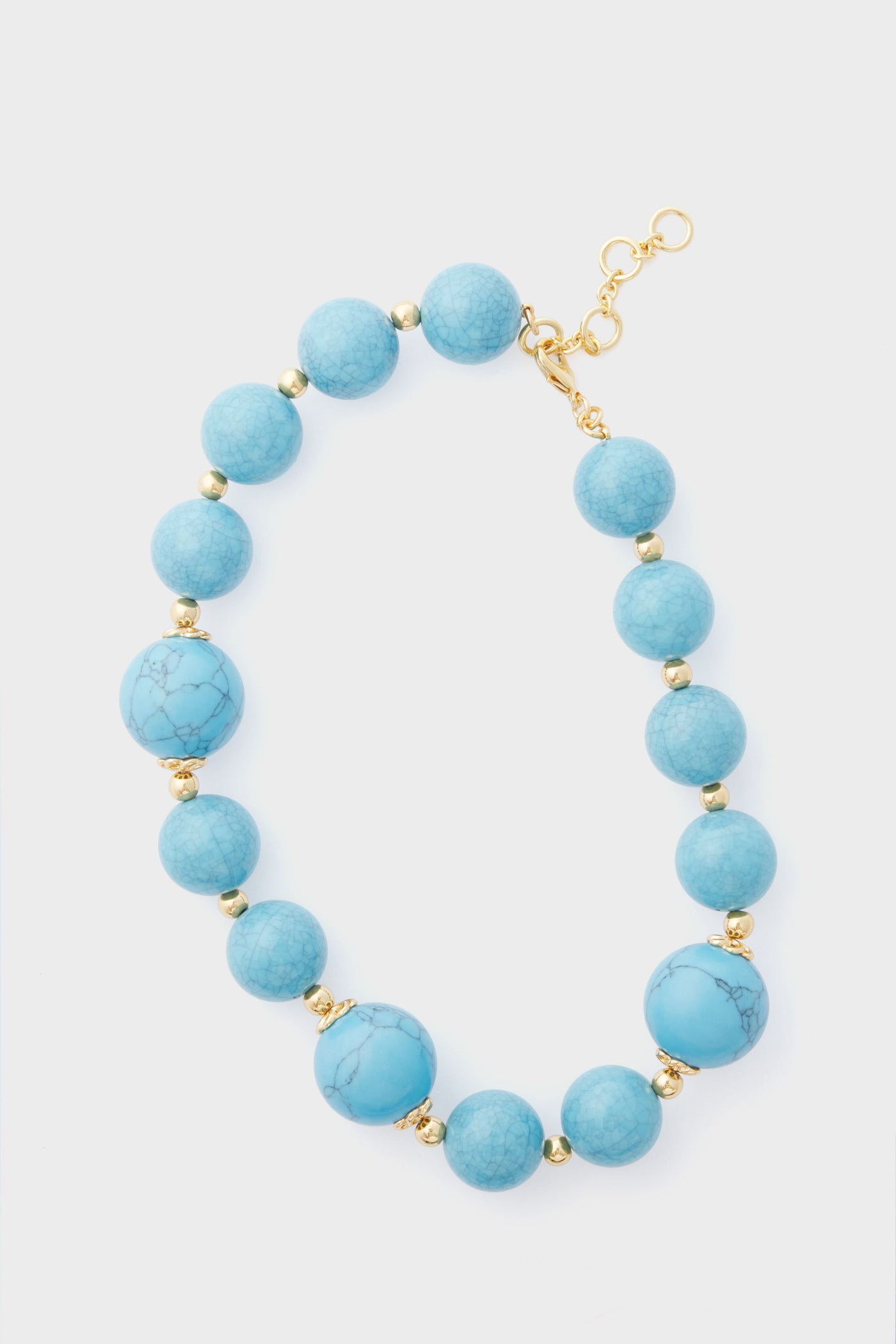 The Tuckernuck Jewelry turquoise beaded necklace features round turquoise and gold beads with a gold clasp, arranged in a semicircle, adding an elegant touch to any outfit.