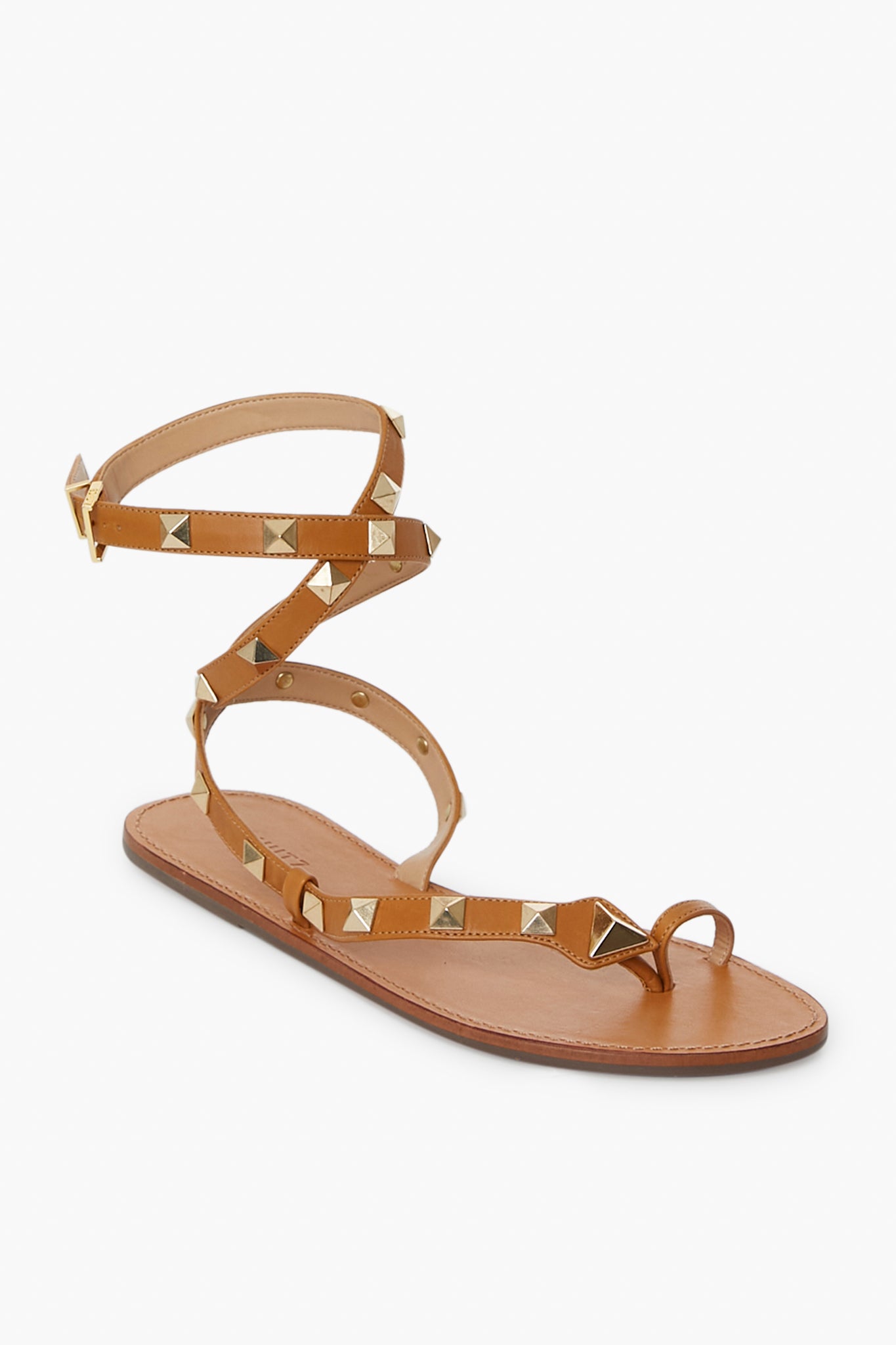 The Schutz tan flat sandal features a toe loop, ankle strap with buckle closure, gold square studs, and a simple leather sole—perfect for everyday wear.