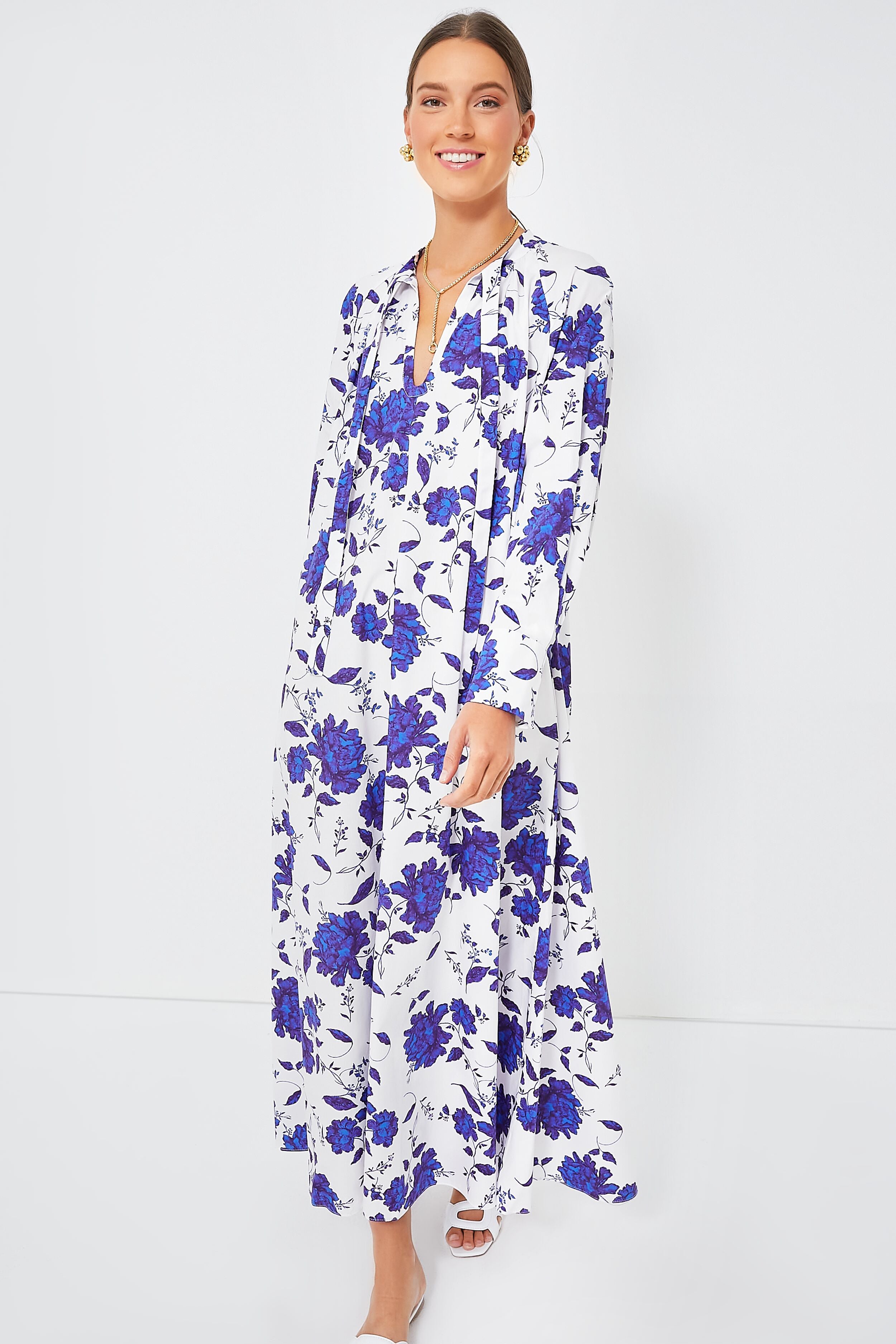 A woman smiles while standing barefoot in an Emilia Wickstead blue floral long-sleeve maxi dress.