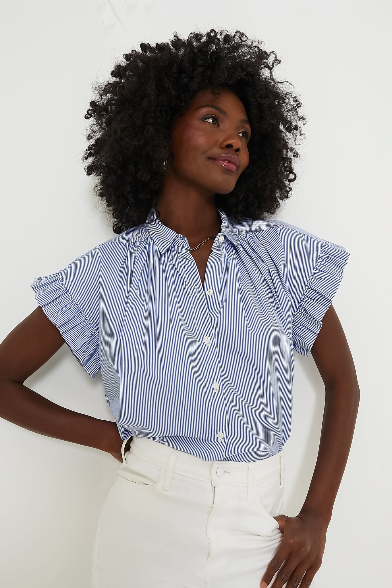 A woman wears a TROVATA Birds of Paradis blue and white striped short-sleeve blouse with ruffled sleeves, paired with white high-waisted pants.