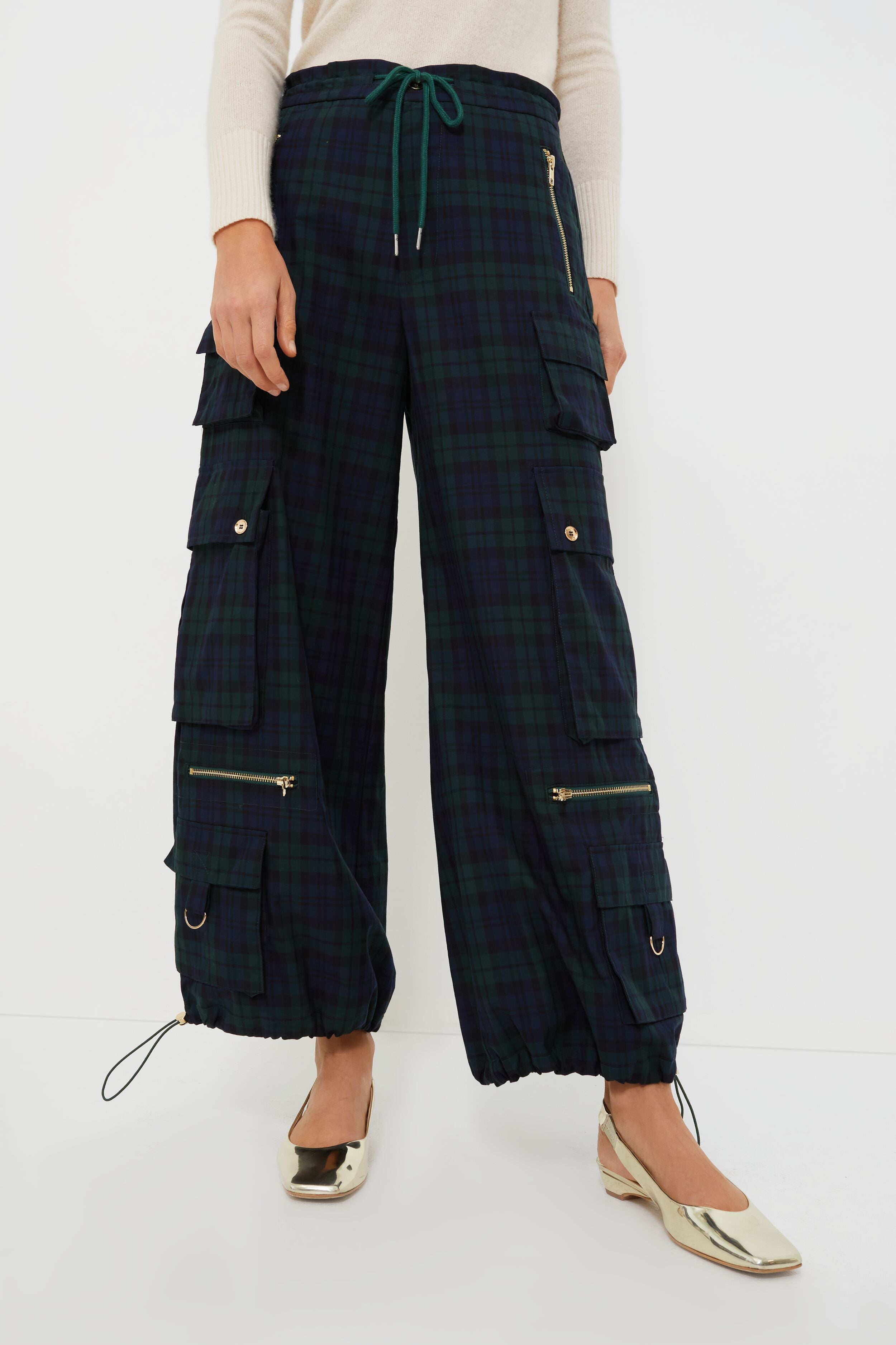 A woman wears Cynthia Rowley wide leg cargo pants in dark Blackwatch Plaid with multiple pockets and zippers, styled with a light sweater and metallic flats—an ideal choice for women’s holiday fashion.