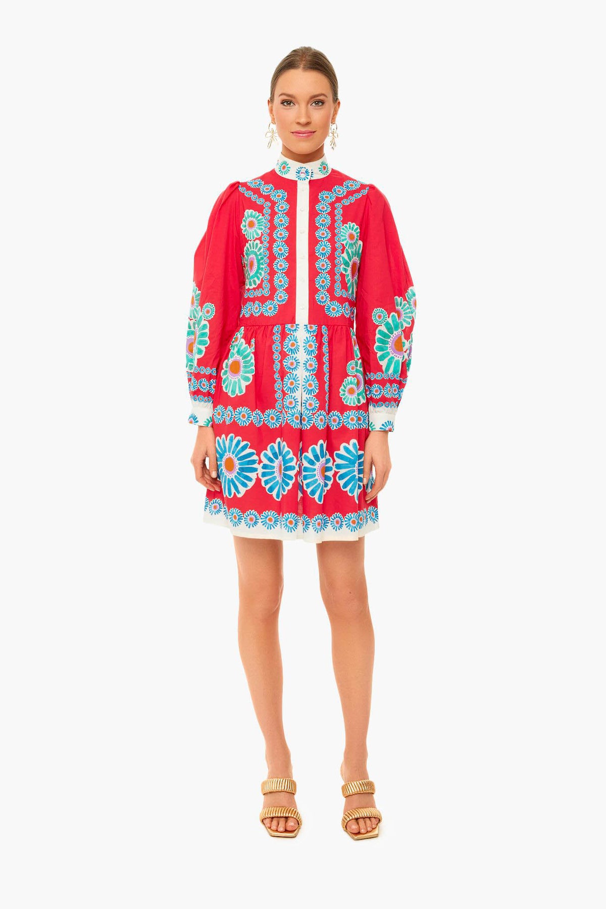 A woman faces forward in a bright red La DoubleJ dress with blue and white floral embroidery, long sleeves, and beige heeled sandals—a Milan-inspired look featuring signature archival prints.