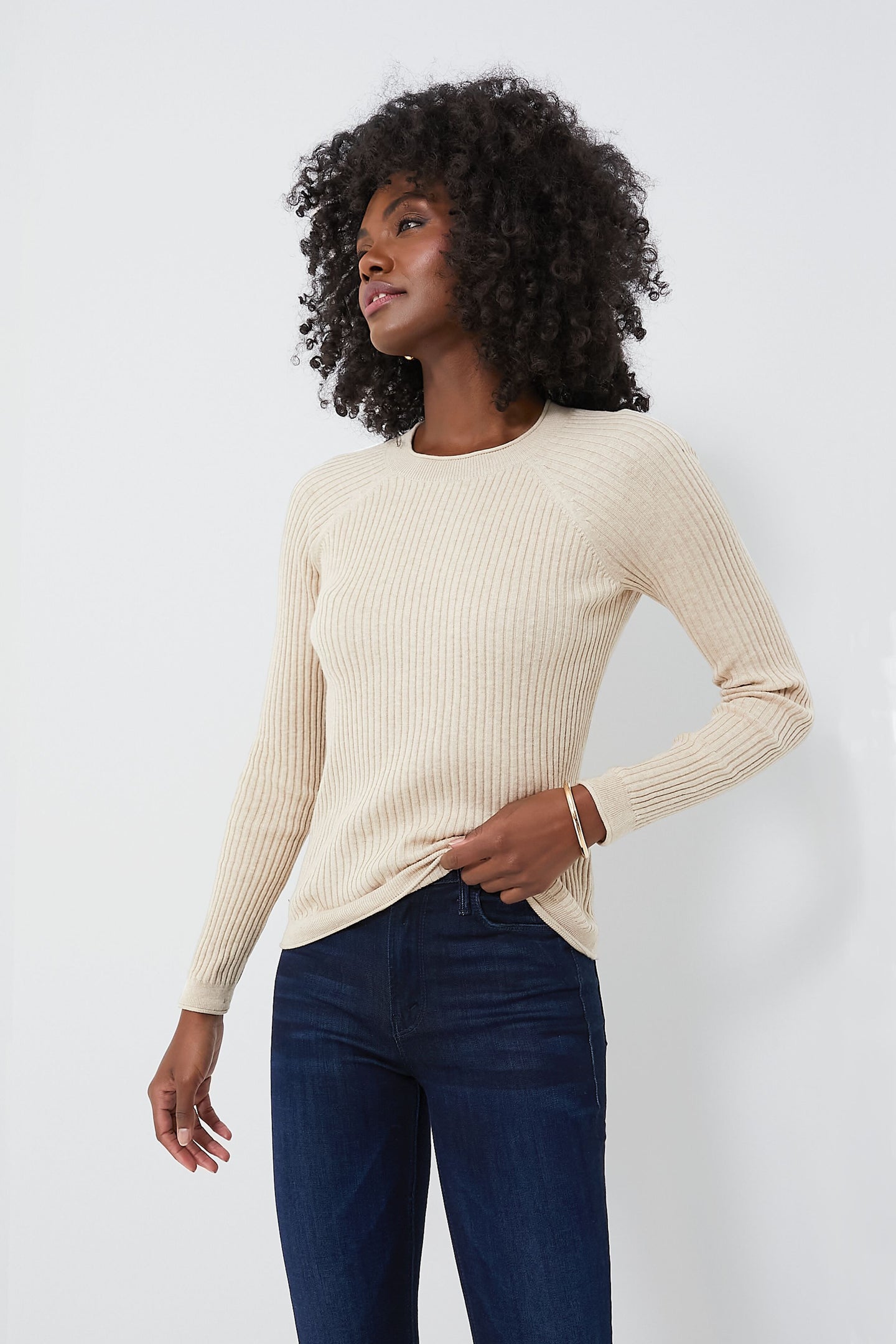 A woman wears a beige Alex Mill crewneck sweater made from cotton-cashmere in a slim fit, paired with dark blue jeans.