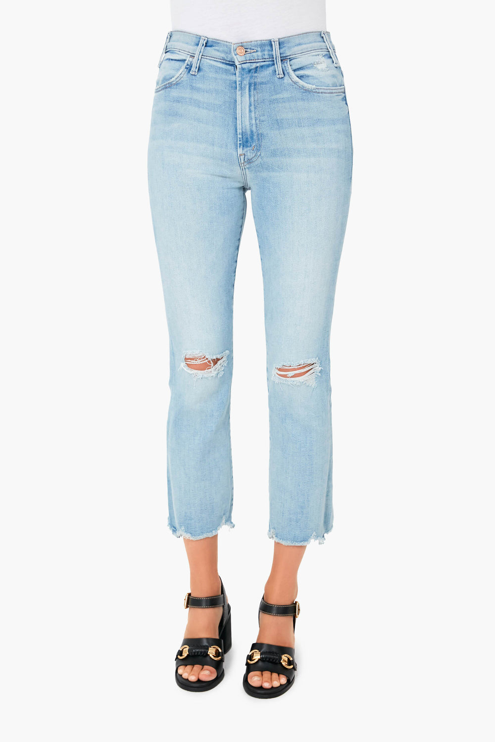 Wearing MOTHER light blue, high-waisted stretch denim cropped jeans with knee rips and frayed hems, paired with black heeled sandals featuring gold accents.