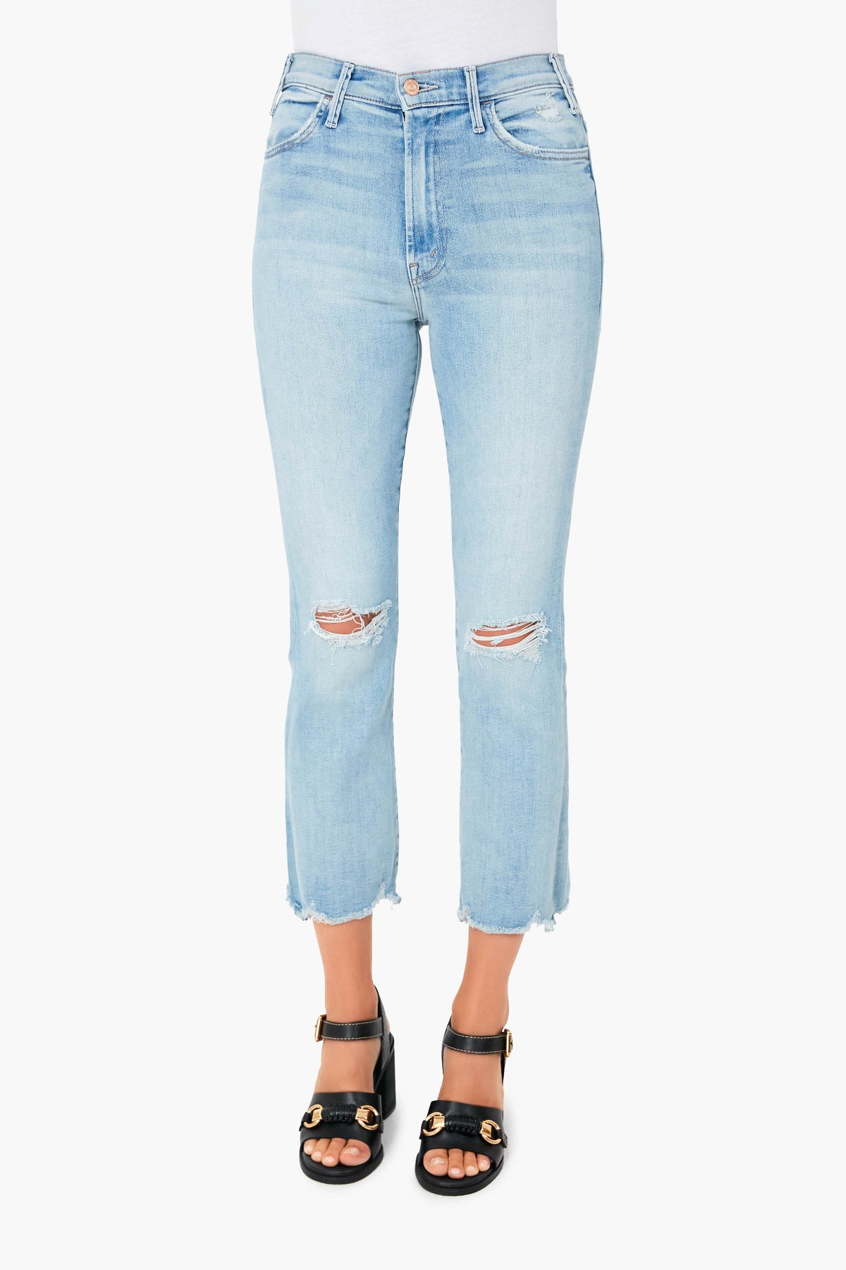 Wearing MOTHER light blue, high-waisted stretch denim cropped jeans with knee rips and frayed hems, paired with black heeled sandals featuring gold accents.