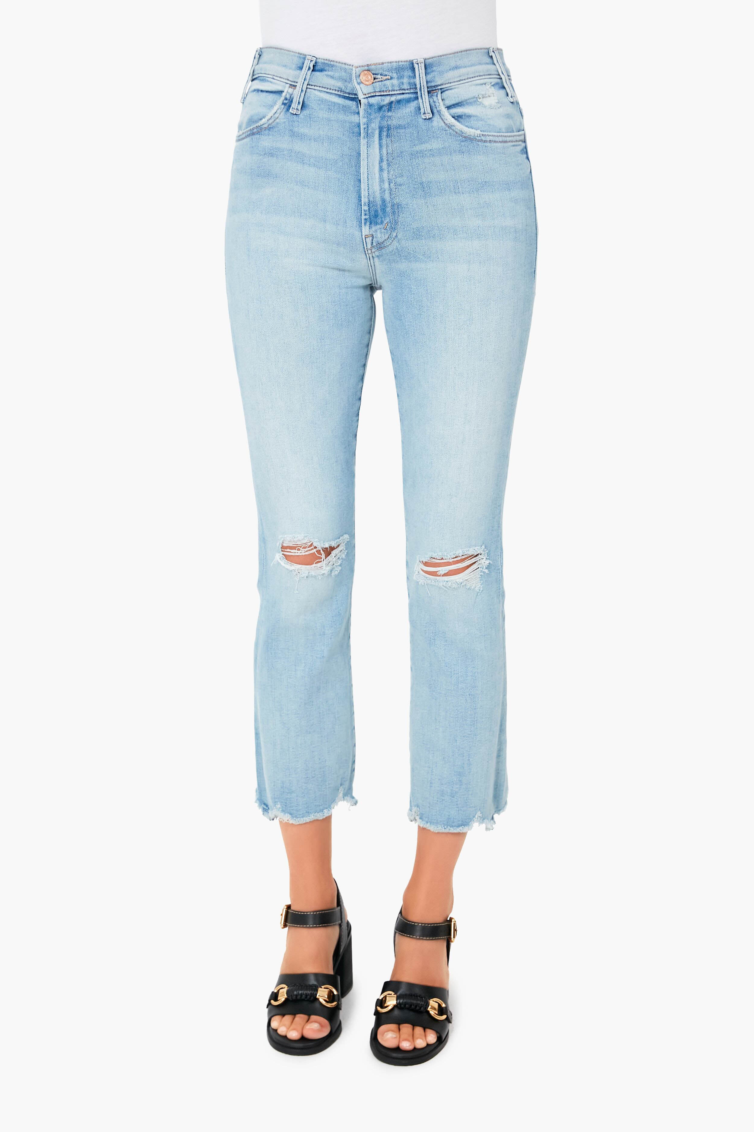 Wearing MOTHER light blue, high-waisted stretch denim cropped jeans with knee rips and frayed hems, paired with black heeled sandals featuring gold accents.