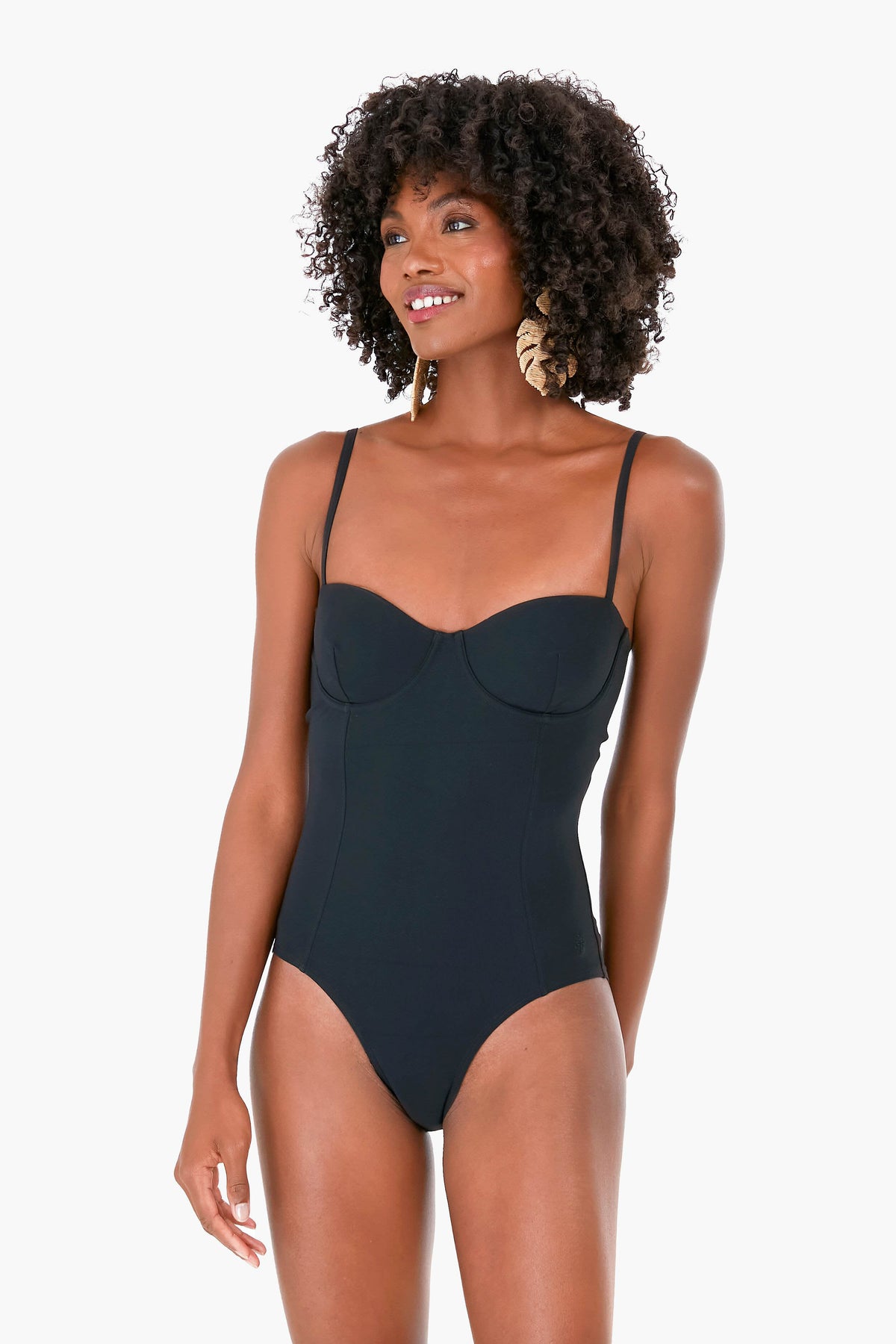 A woman stands confidently wearing a Tory Burch black underwire one-piece swimsuit with thin straps.