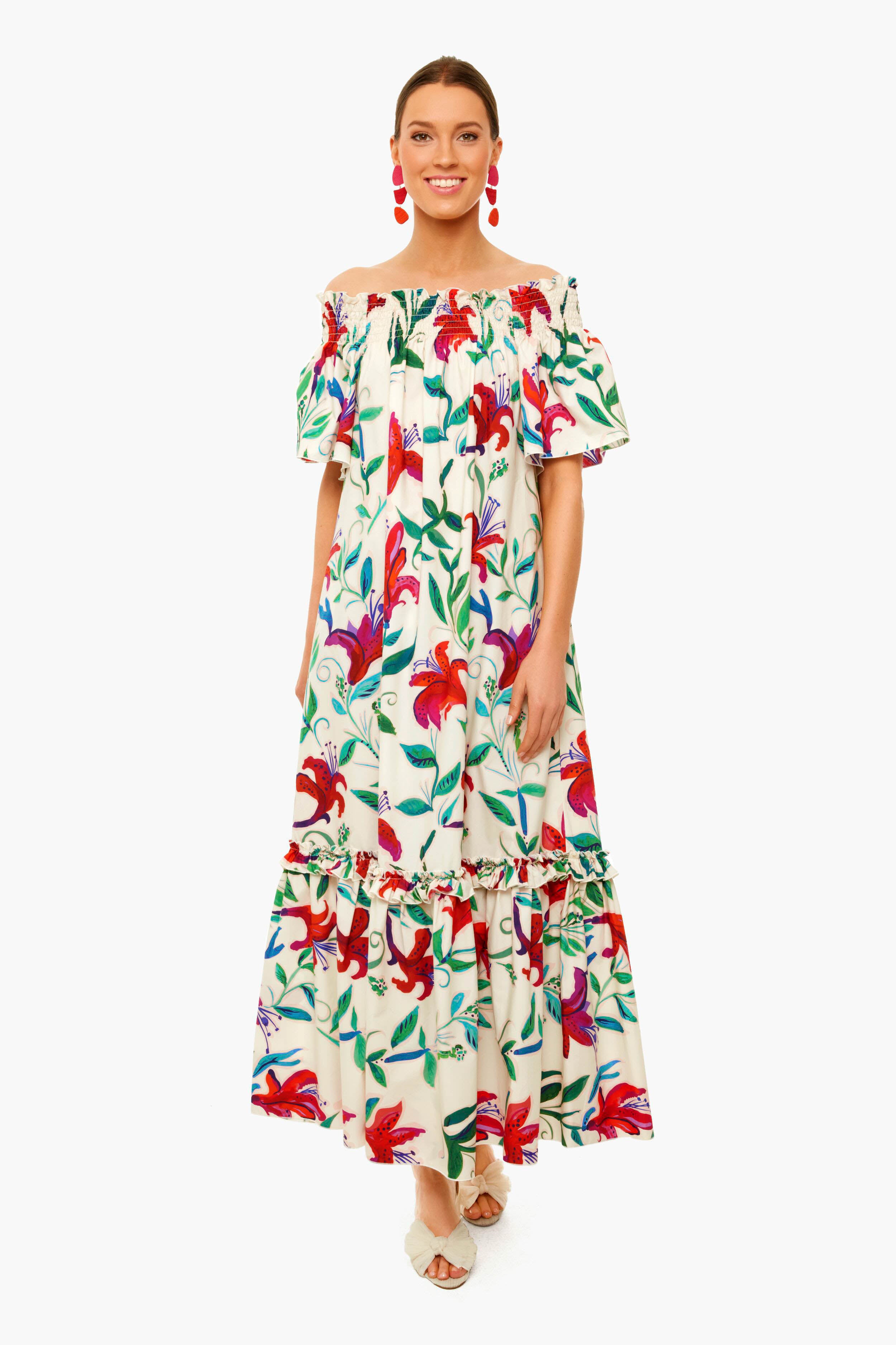 A woman wears a La DoubleJ Capalbio Dress in vibrant floral cotton poplin, styled with red statement earrings and white open-toe shoes.