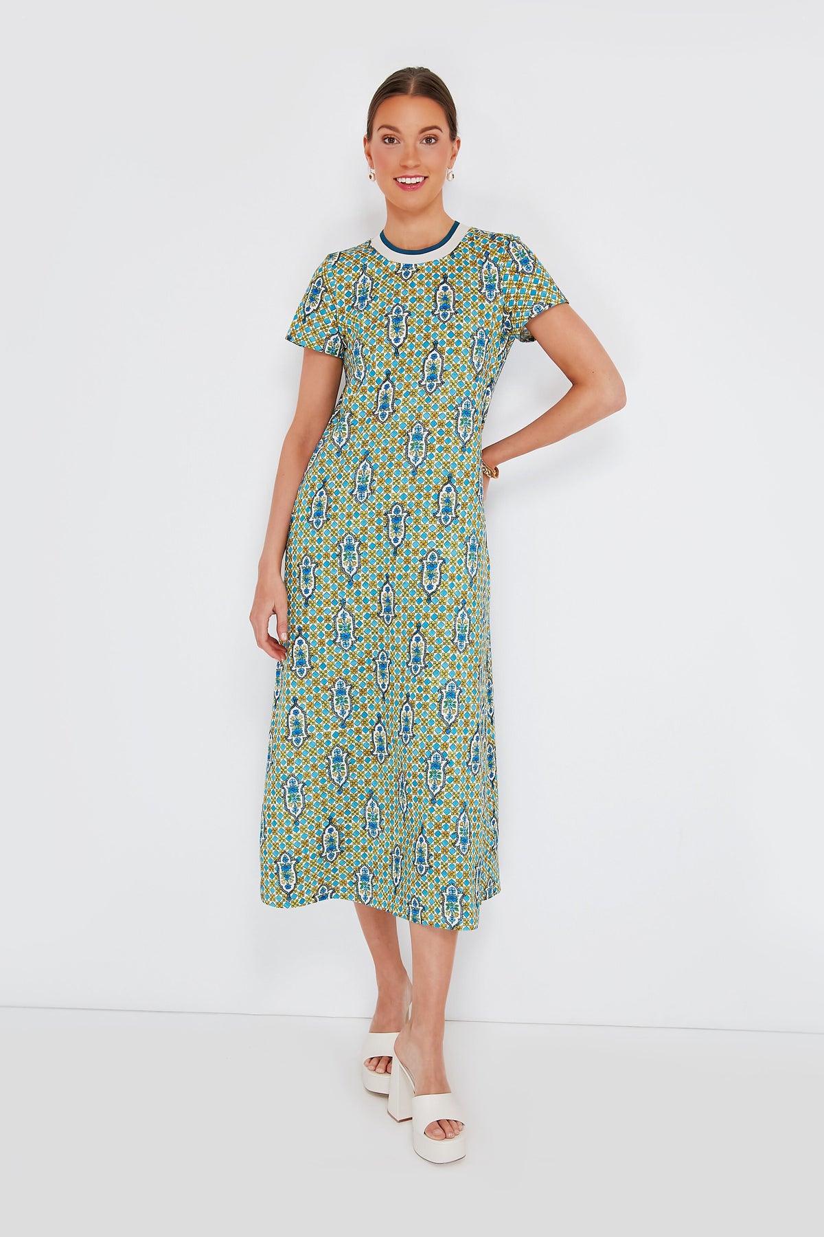 Woman in a patterned green and blue La DoubleJ Sporty Swing Dress made in Italy stands smiling with one hand on her hip, wearing white platform sandals.