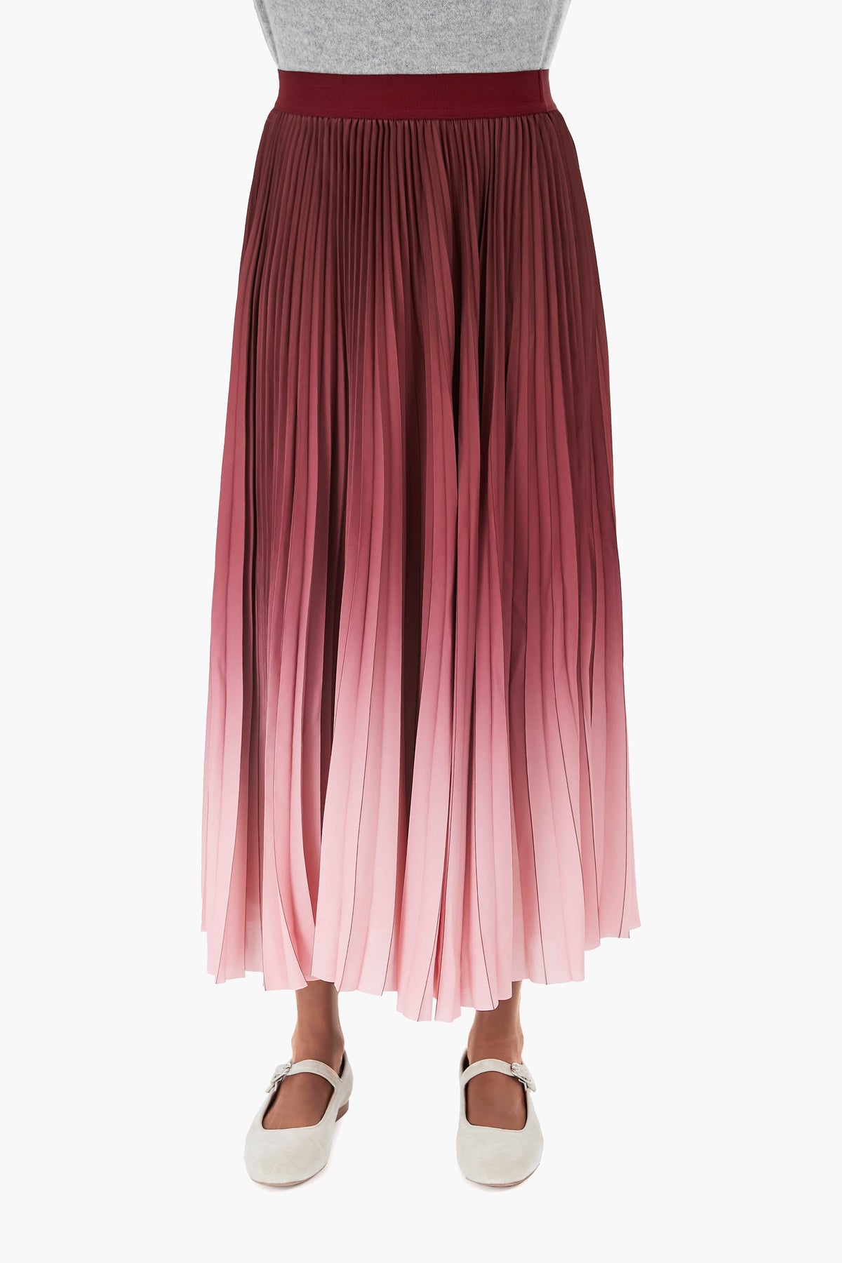 A person wears a gray top, a pleated midi skirt with a pink and burgundy gradient print by Weekend Max Mara, and white strapped shoes.