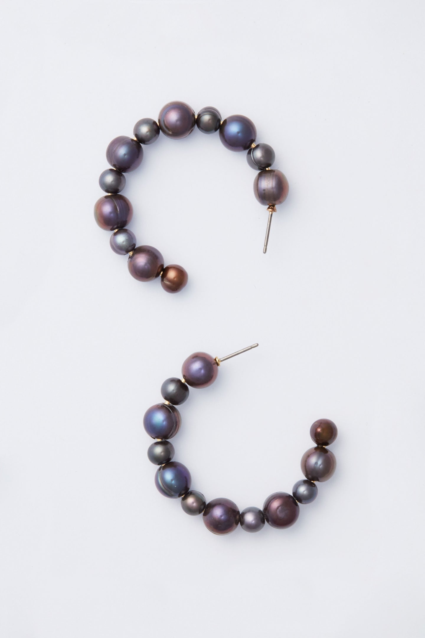 A pair of open gold hoop earrings with round, iridescent dark pearls in a half-circle design—an elegant piece by Tuckernuck Jewelry.