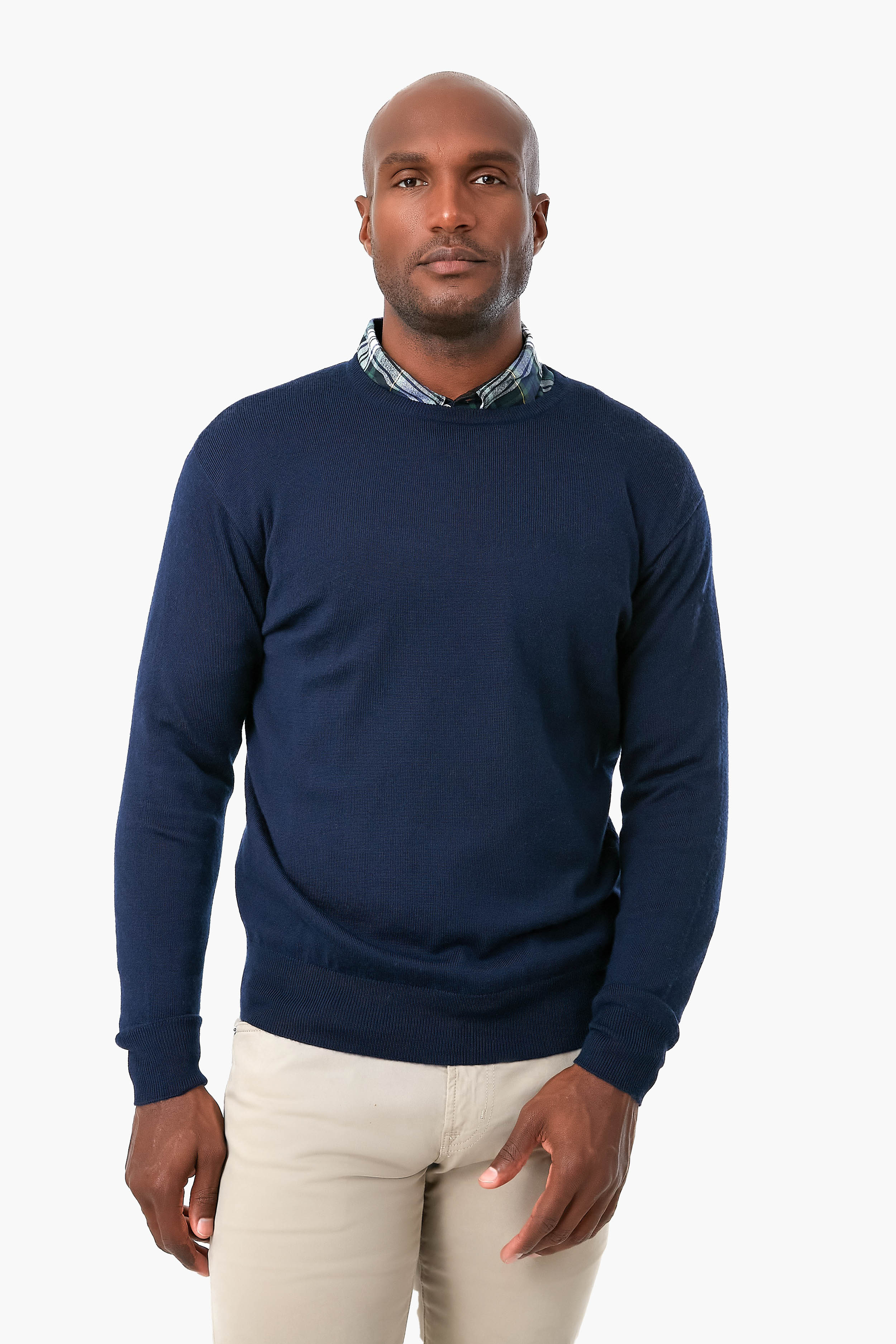 A man wears a navy blue Peter Millar sweater with a patterned collared shirt and beige pants.