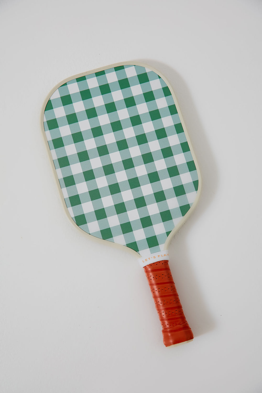 The Tnuck Sport x Recess Pickleball paddle features a green and white checkered design, an orange grip handle, and a honeycomb core for enhanced performance.