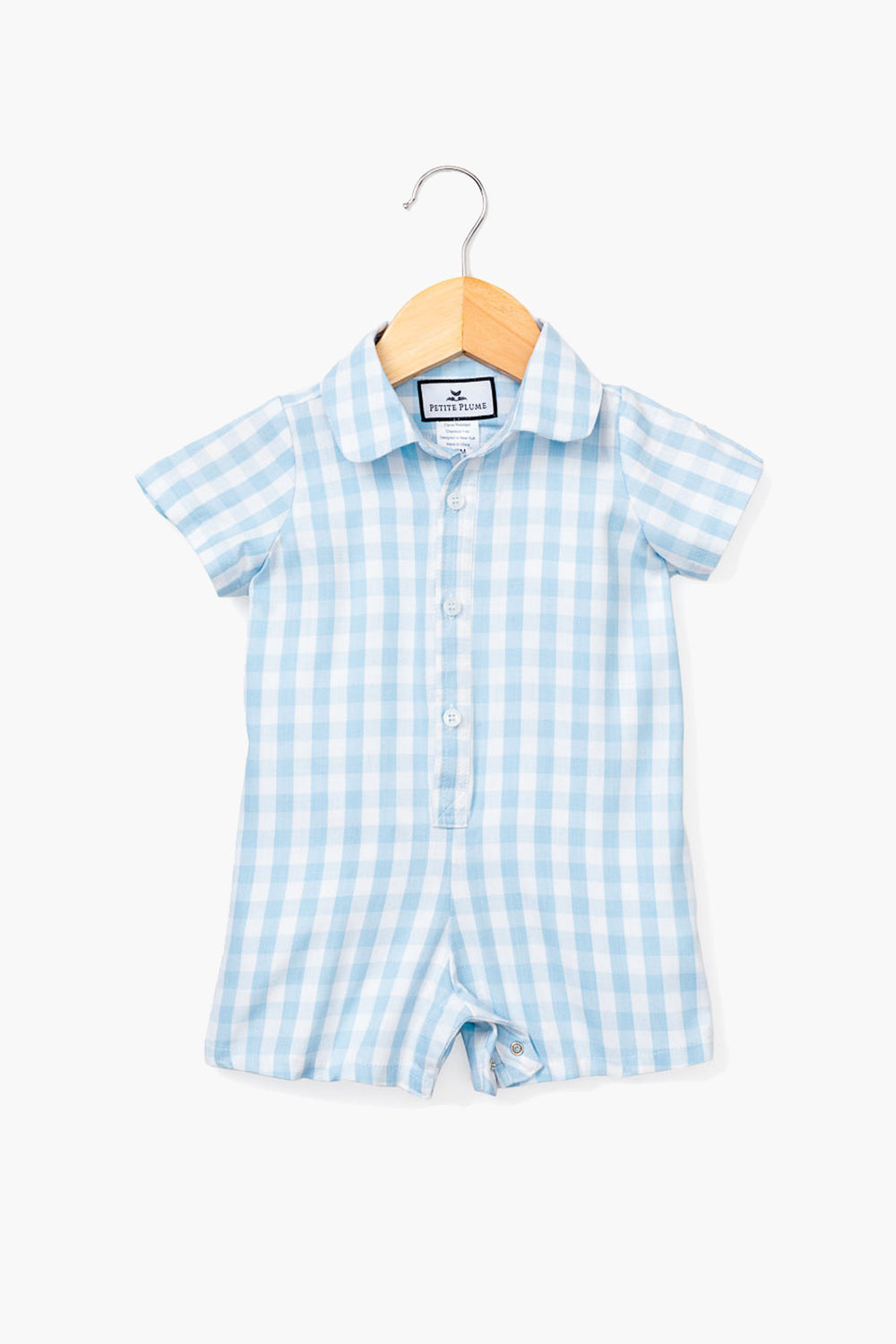 A Petite Plume short-sleeve blue gingham infant romper with a button front and collar, crafted from soft cotton sleepwear, is displayed on a wooden hanger.