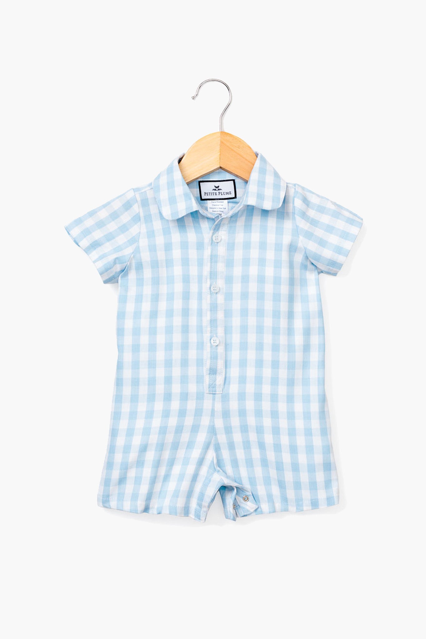 A Petite Plume short-sleeve blue gingham infant romper with a button front and collar, crafted from soft cotton sleepwear, is displayed on a wooden hanger.