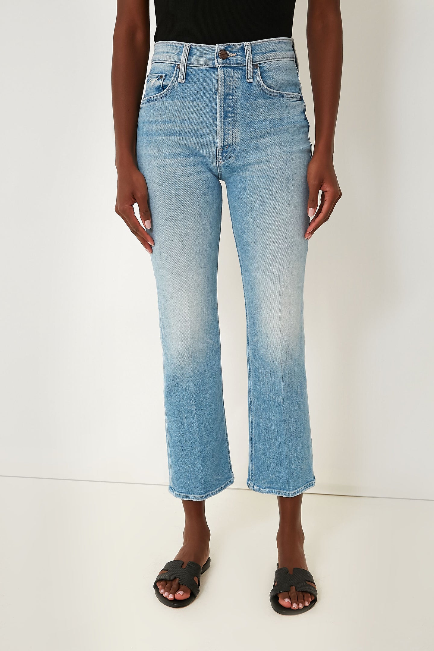 A person wearing MOTHER light blue ankle-length jeans, a black sleeveless top, and black open-toe sandals.
