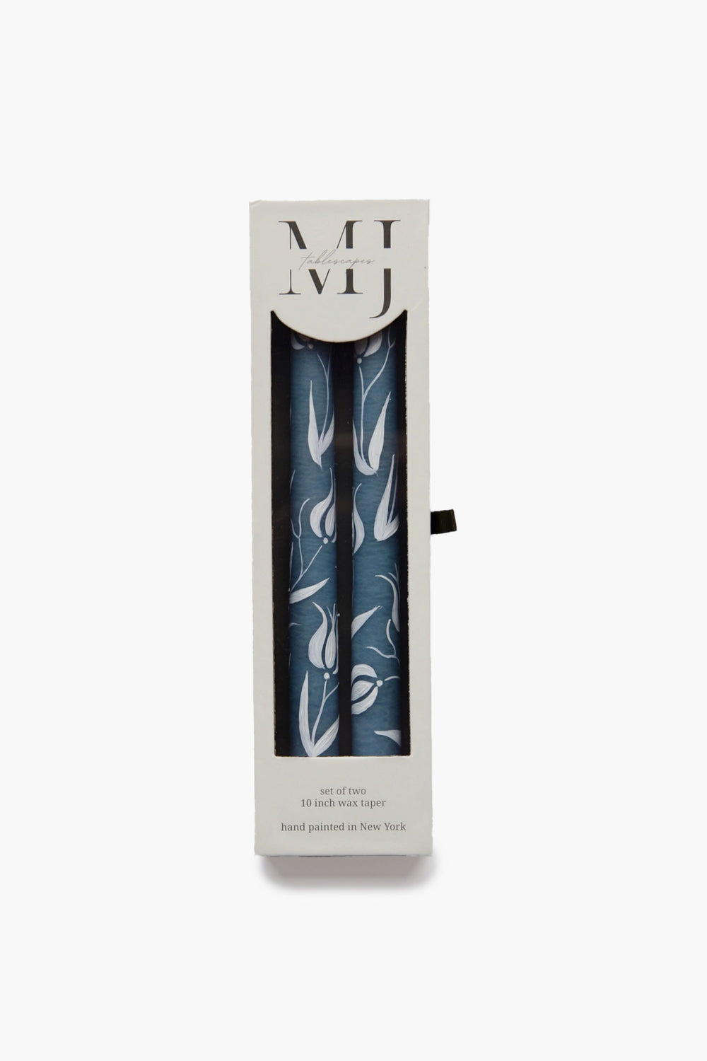 A box of two blue tulip candles with a white floral pattern from MJ Tablescapes, partially visible through a clear window. The packaging features printed text and MJ Tablescapes branding.
